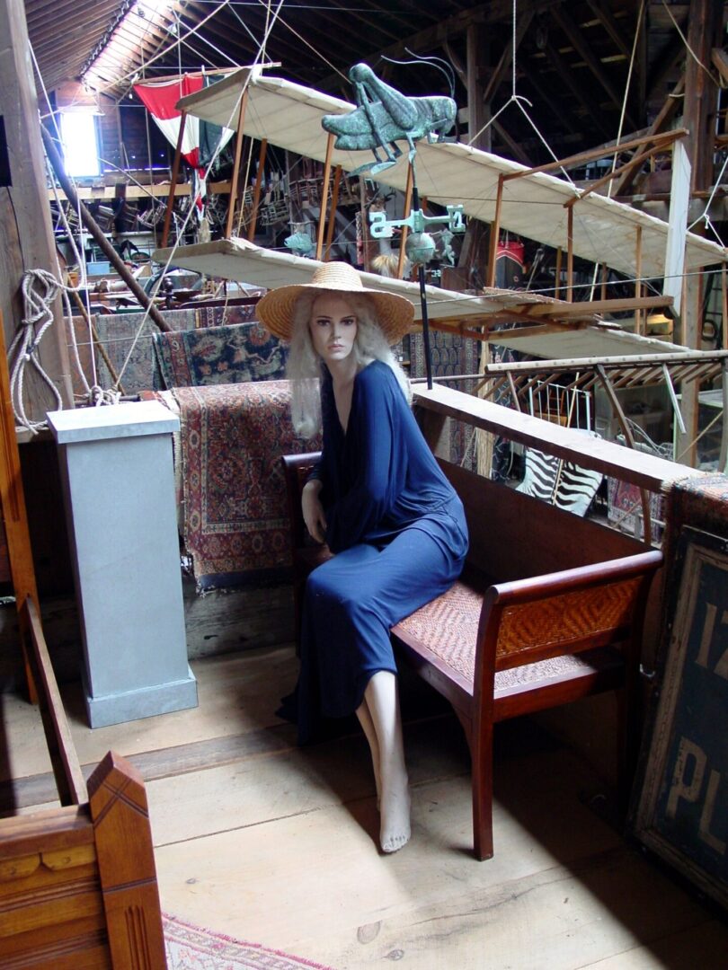 Mannequin dressed in blue sitting on a wooden chair on a ship deck.