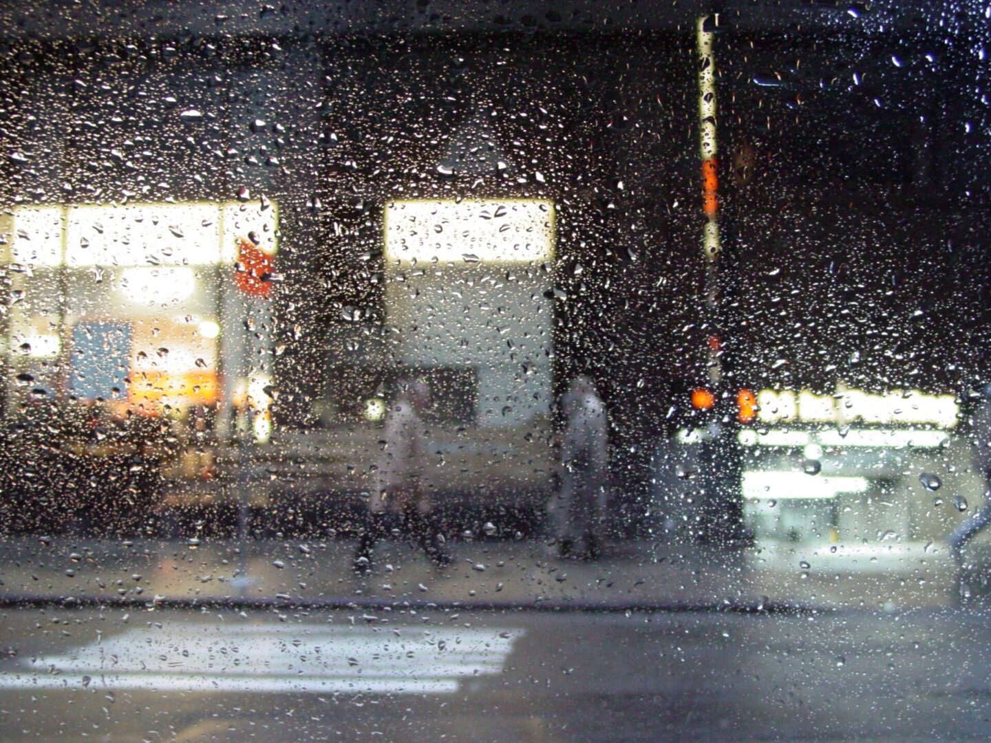 View of a rainy street through a water-covered window at night.