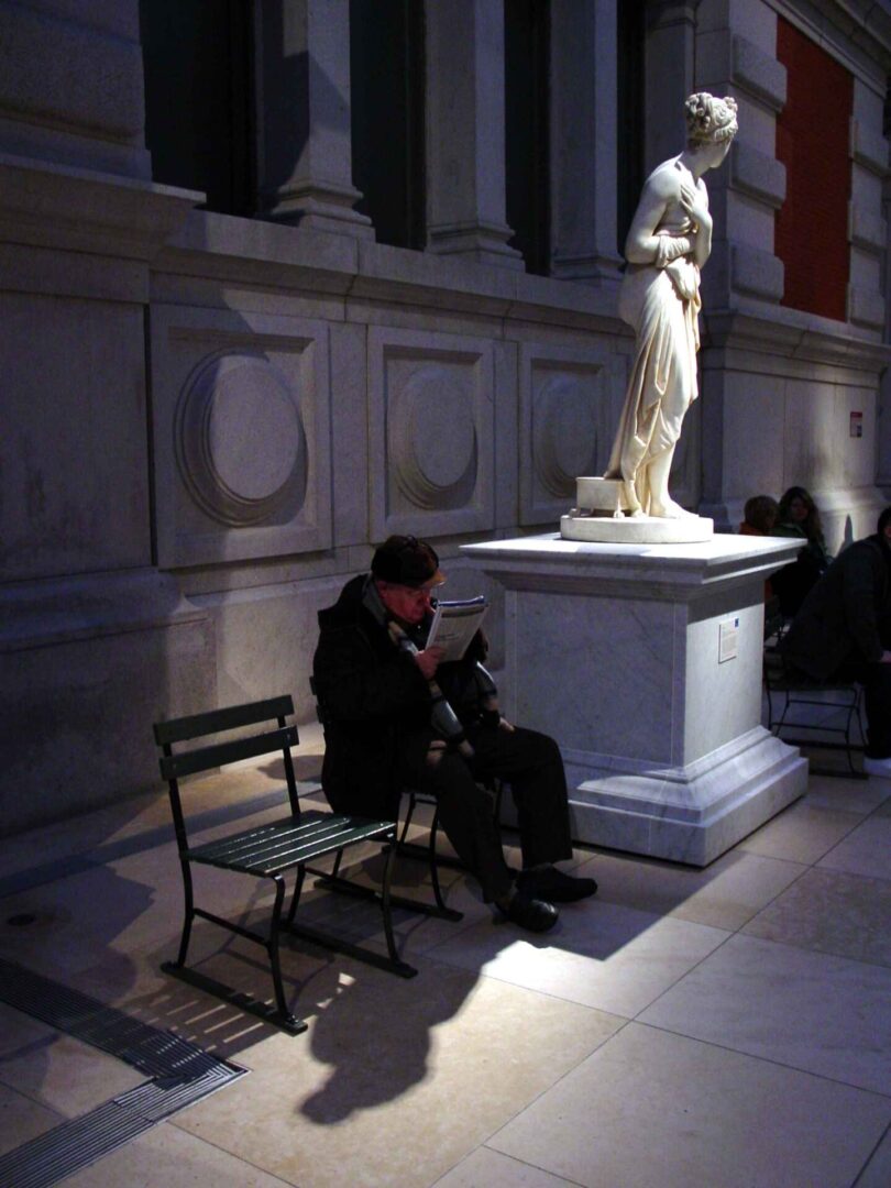 Man sitting on a chair playing a musical instrument near a statue indoors.