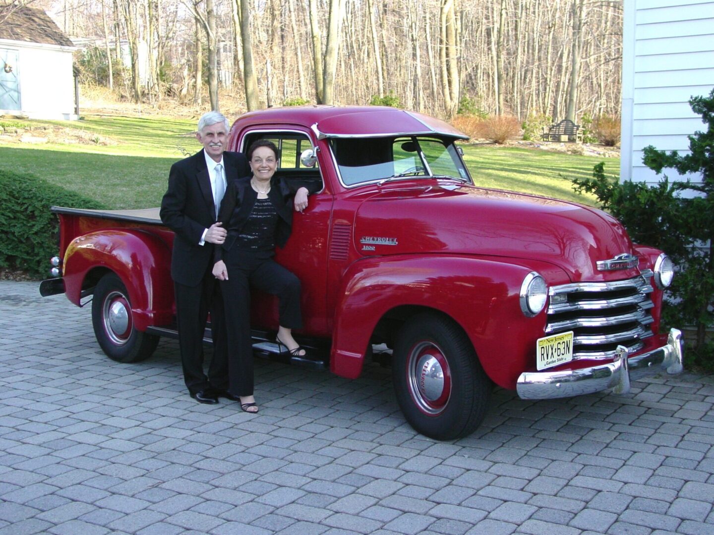 A couple posing beside a vintage red pickup truck on a sunny day.