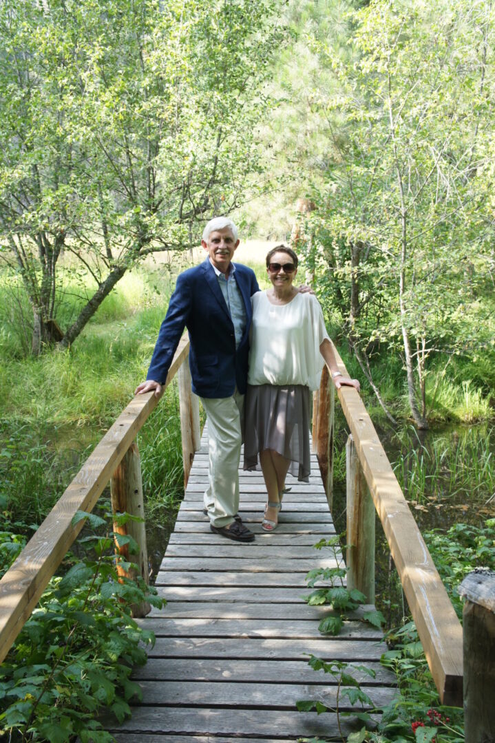 A couple walking hand in hand on a wooden bridge in a green park.
