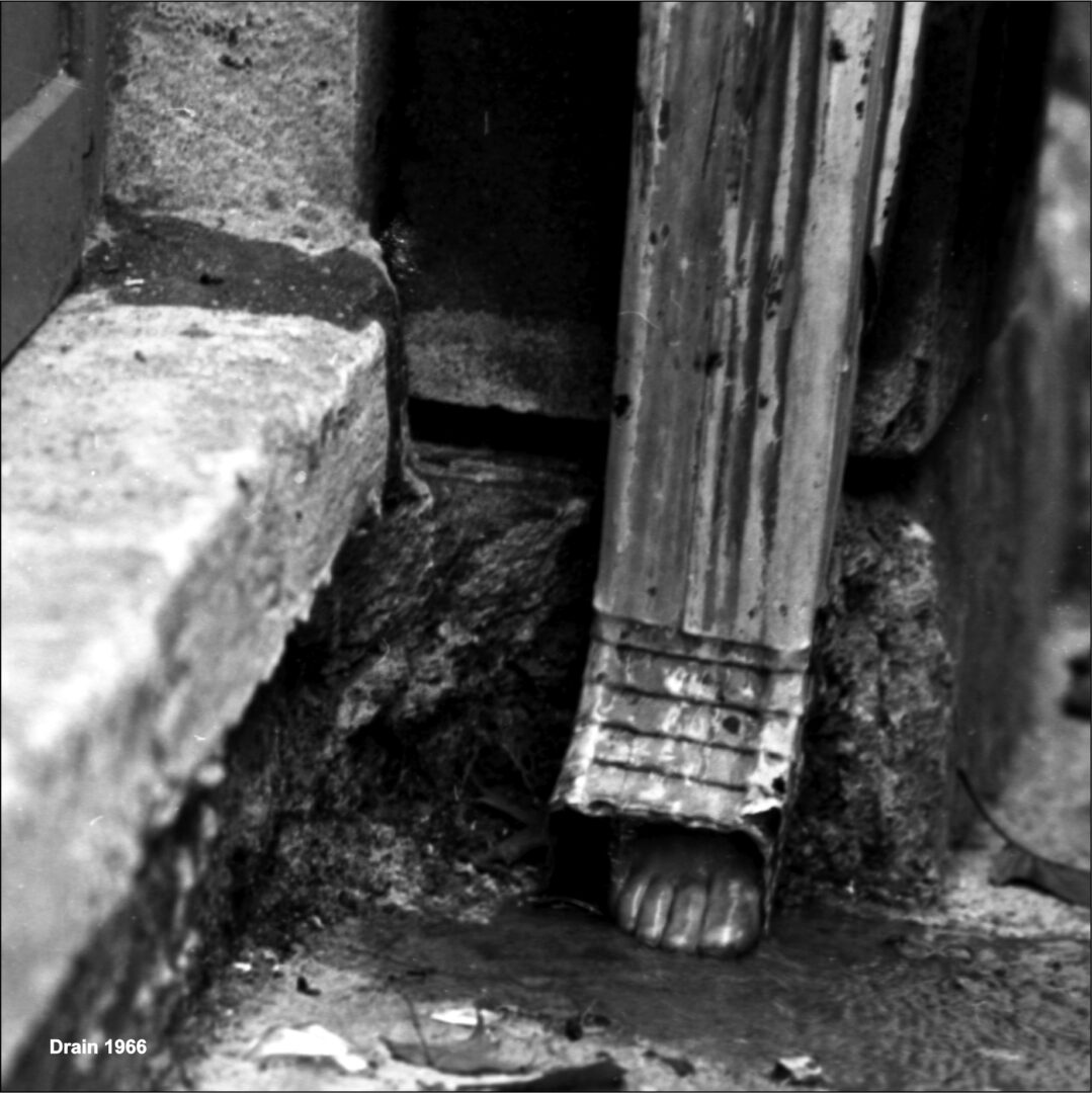 Close-up of a weathered gutter downspout and cracked concrete surface.