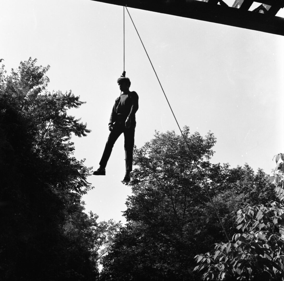 A person hanging by a rope under a bridge in a black and white photo.