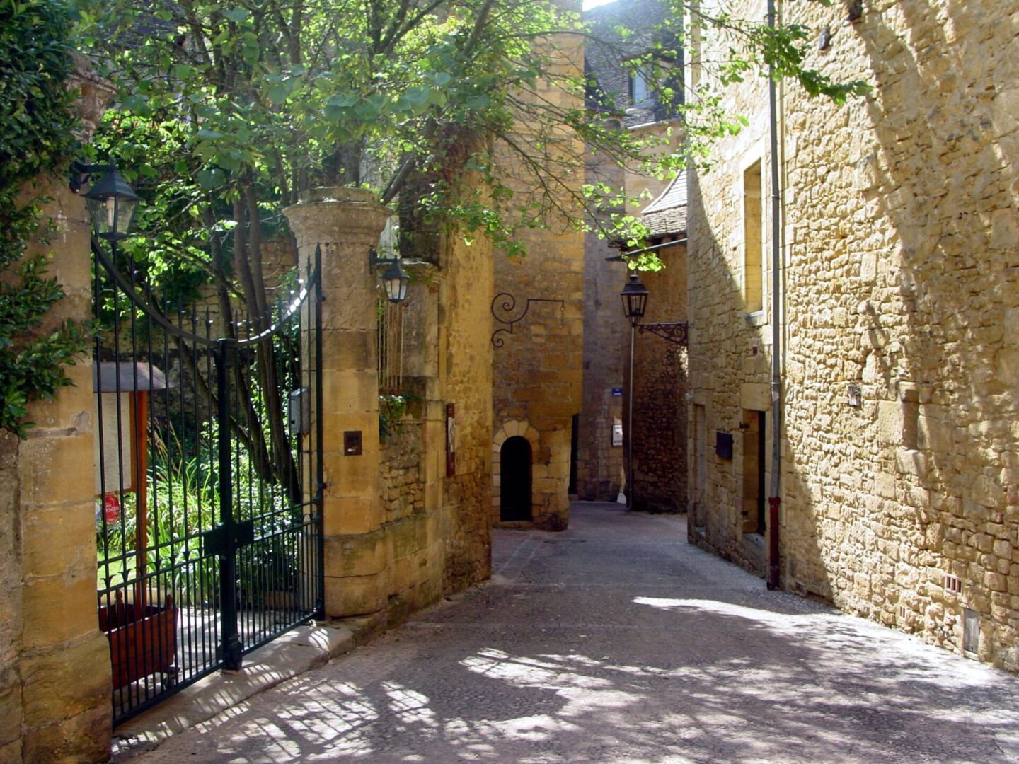 Quaint stone alleyway bathed in sunlight with greenery and an iron gate.