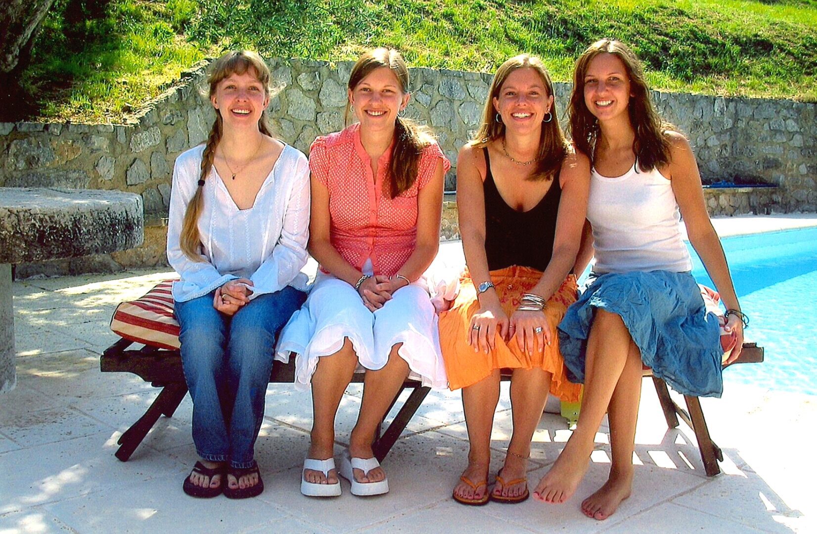 Four women sitting outdoors, smiling and enjoying a sunny day.