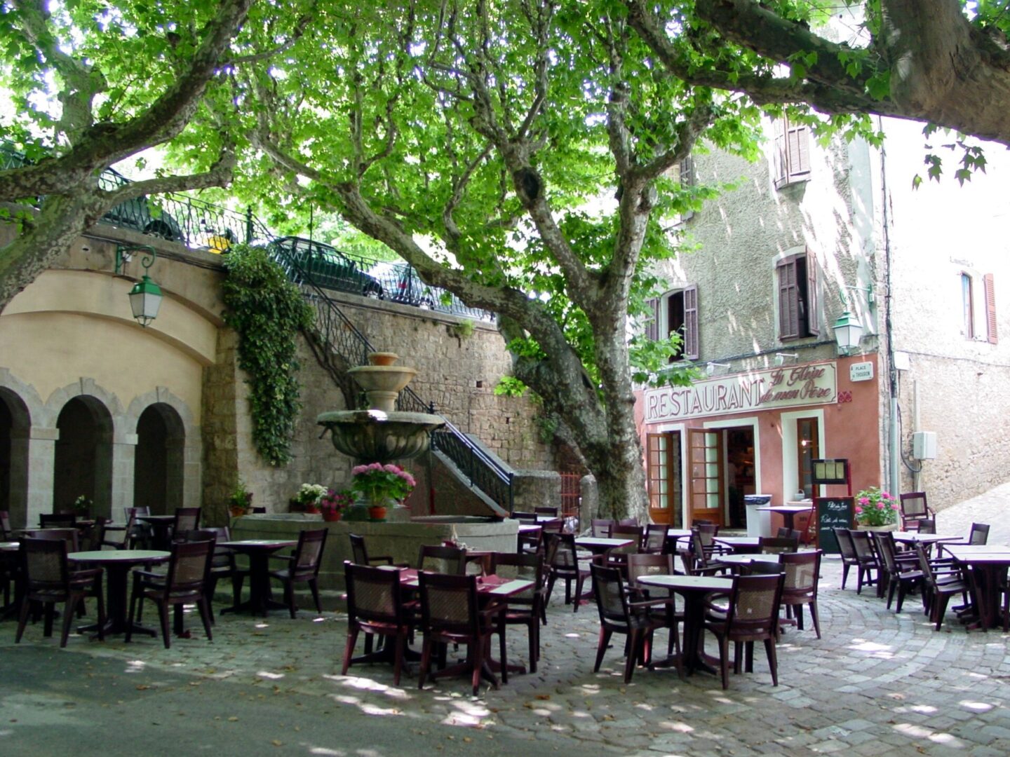 Charming outdoor café seating under lush green trees in a quaint courtyard.