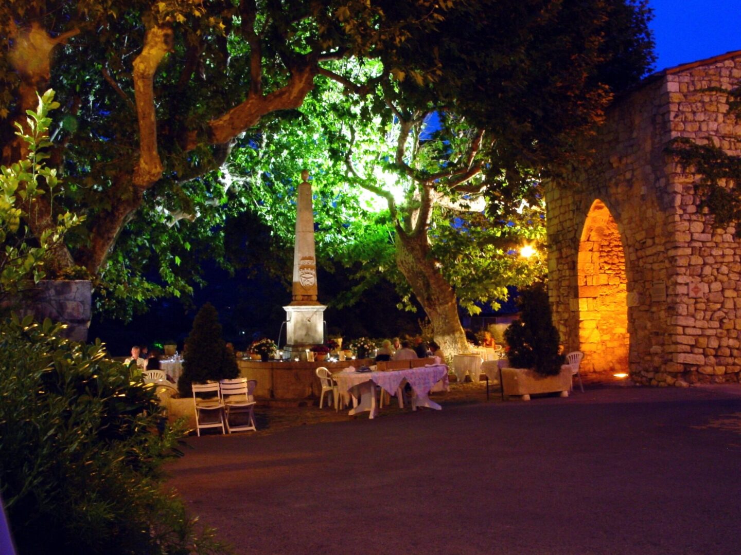 Cozy outdoor dining area illuminated by warm lights under a large tree at night.