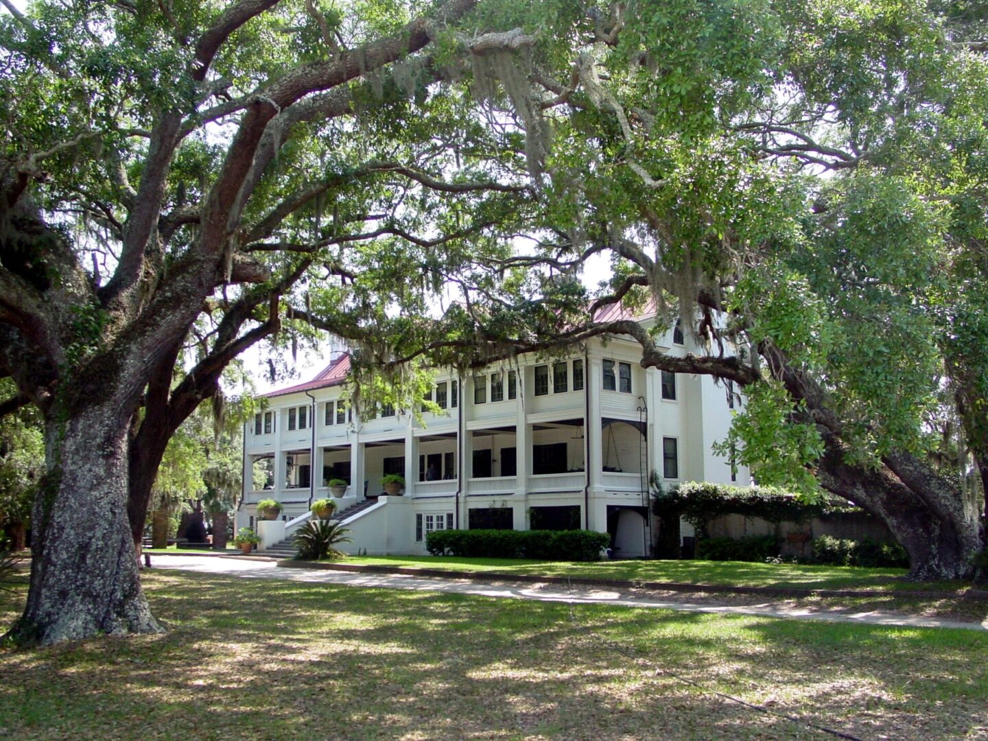 Historic white building surrounded by large trees and green lawn.