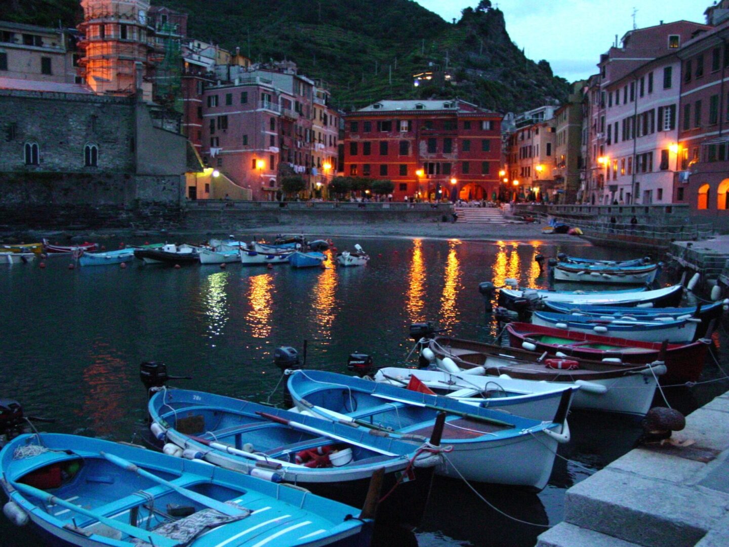 Boats docked at a serene harbor during twilight with colorful buildings in the background.