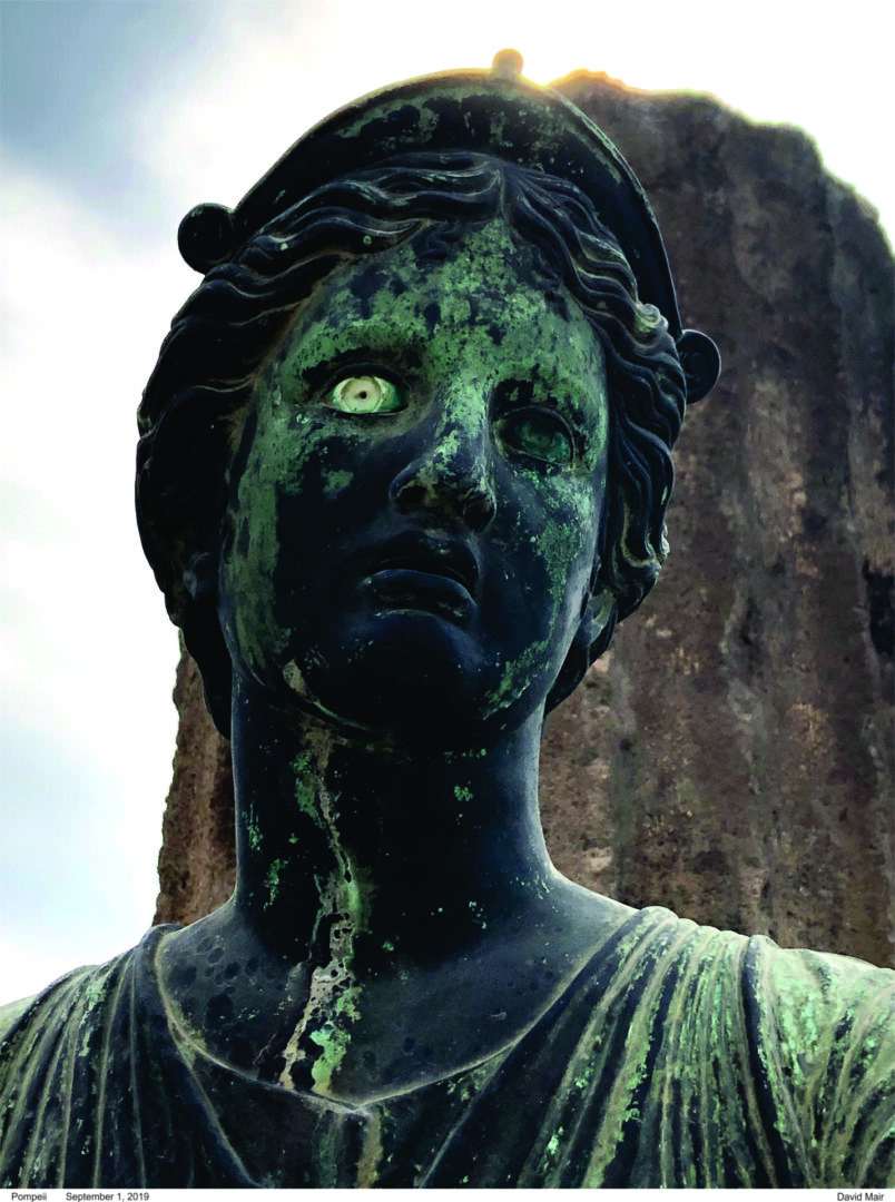 Close-up of a weathered statue with green patina and glowing eyes.