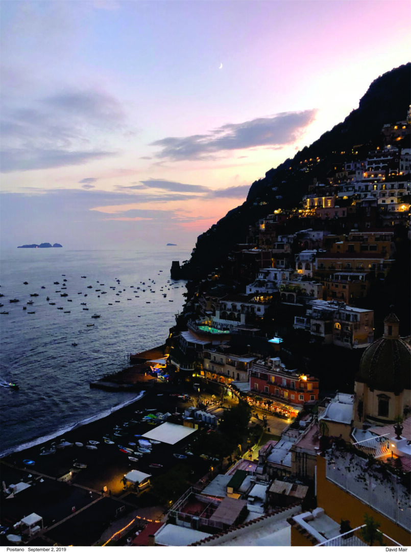 Sunset over a coastal town with lights glowing on the hillside.