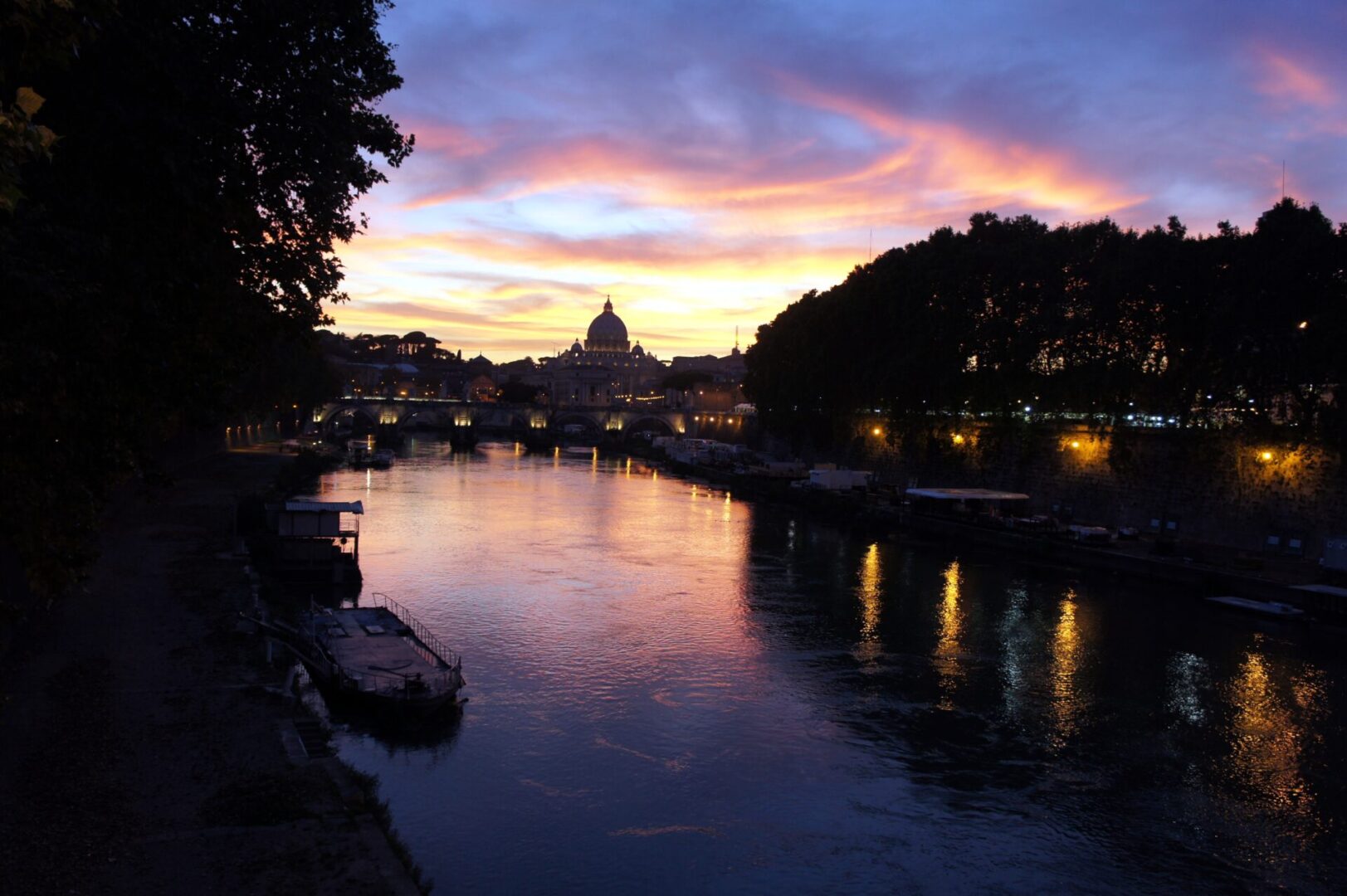 Sunset over a river with a cityscape silhouette including a dome.