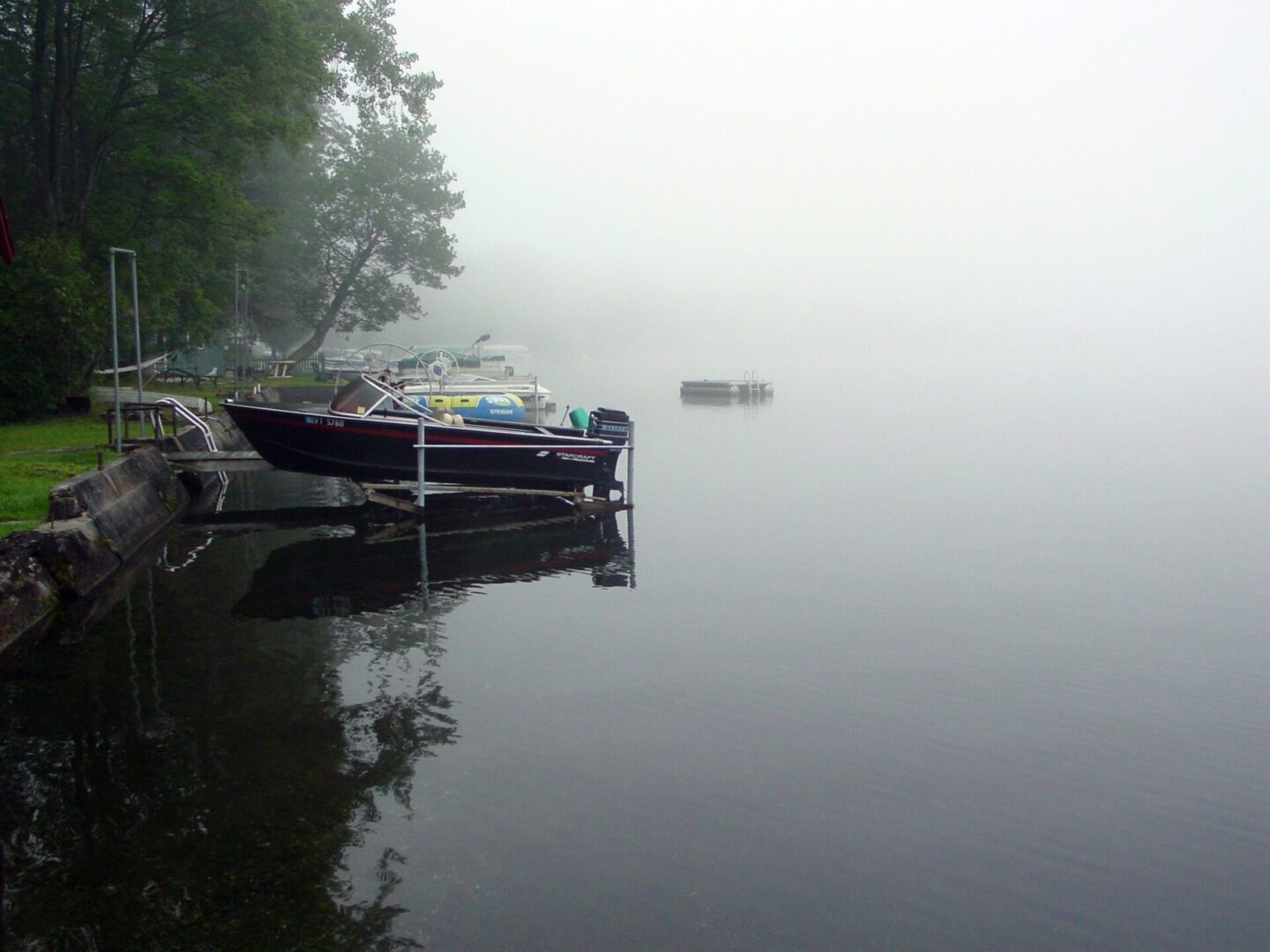 A misty lake with boats docked and calm water reflecting the foggy sky.