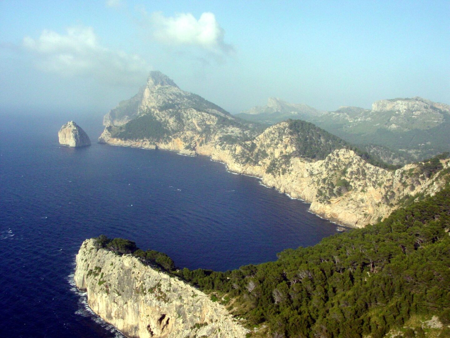 Scenic coastal cliffs overlooking a deep blue sea under a partly cloudy sky.