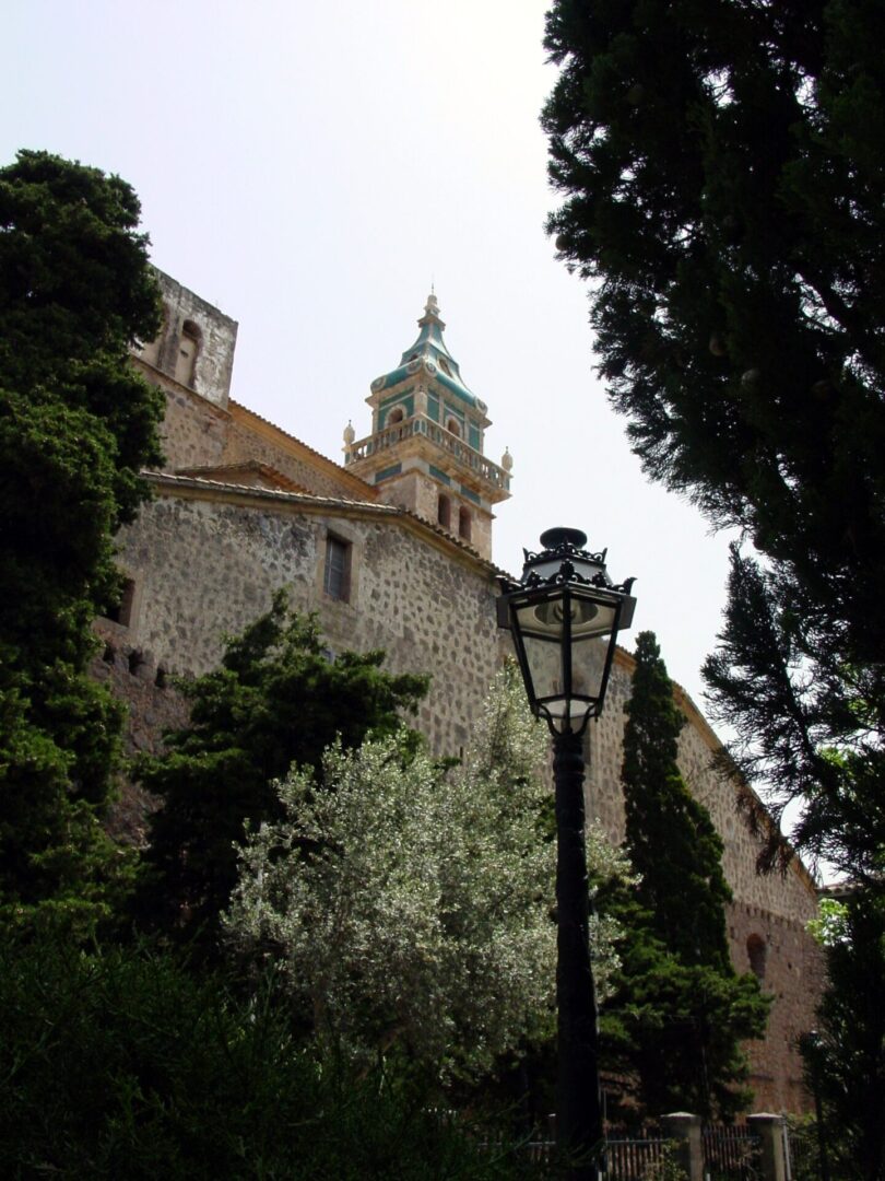 Historic church tower partially hidden by trees and lamppost.