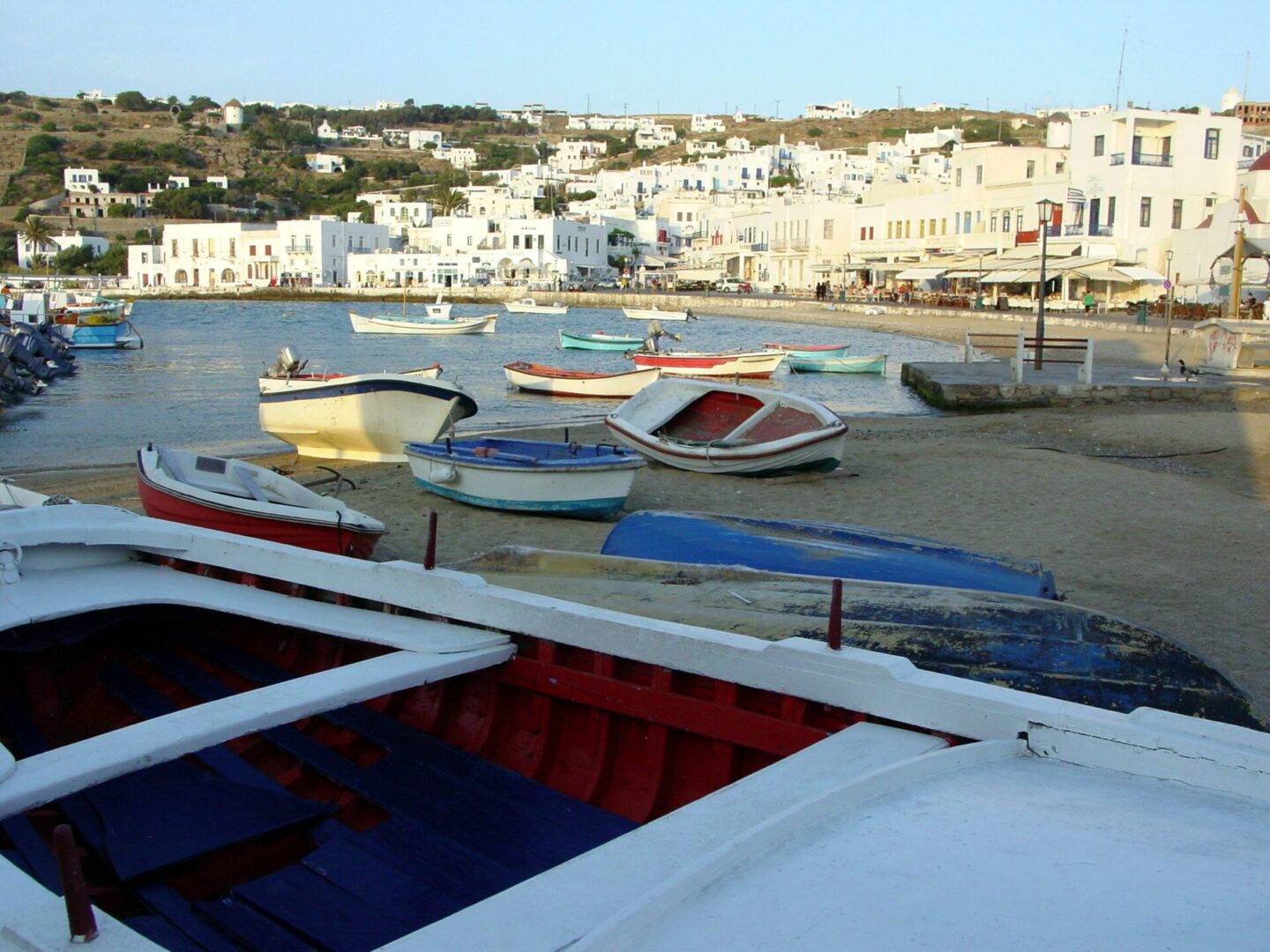 Boats docked by a calm harbor with white buildings in the background.