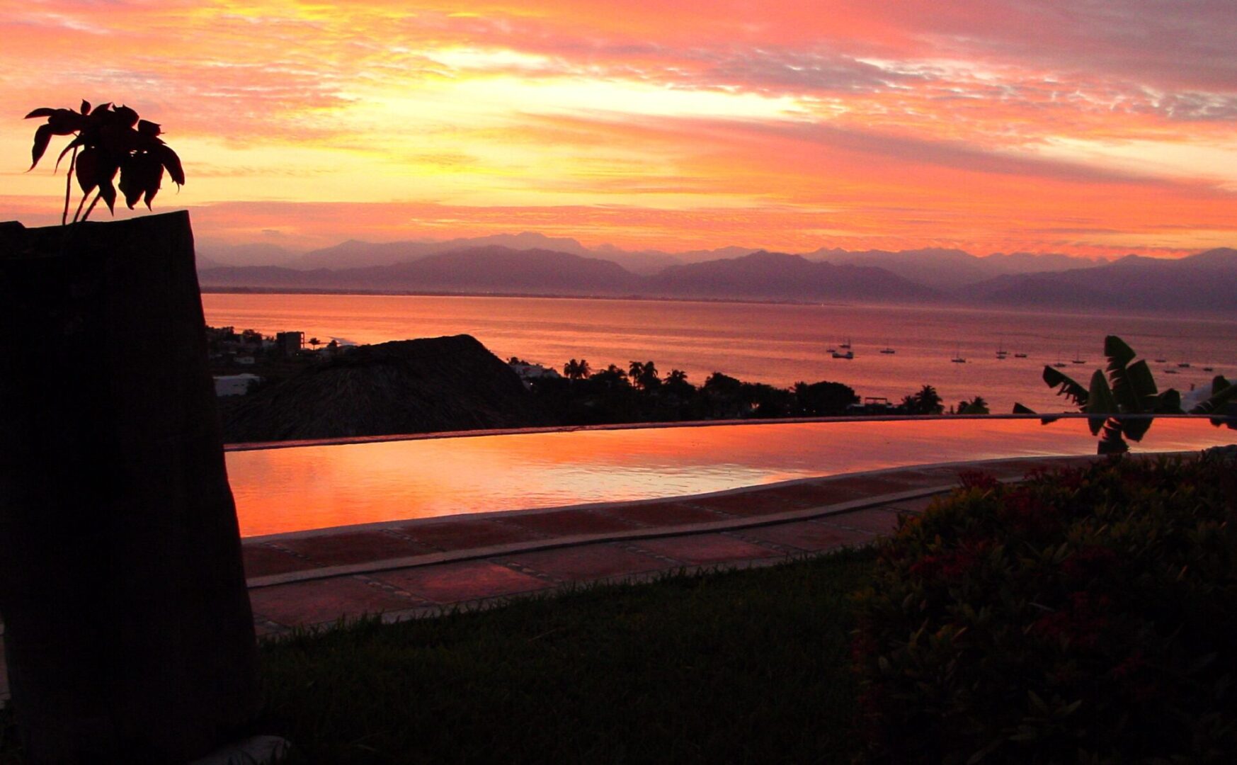 A serene sunset over a calm body of water with silhouetted land.