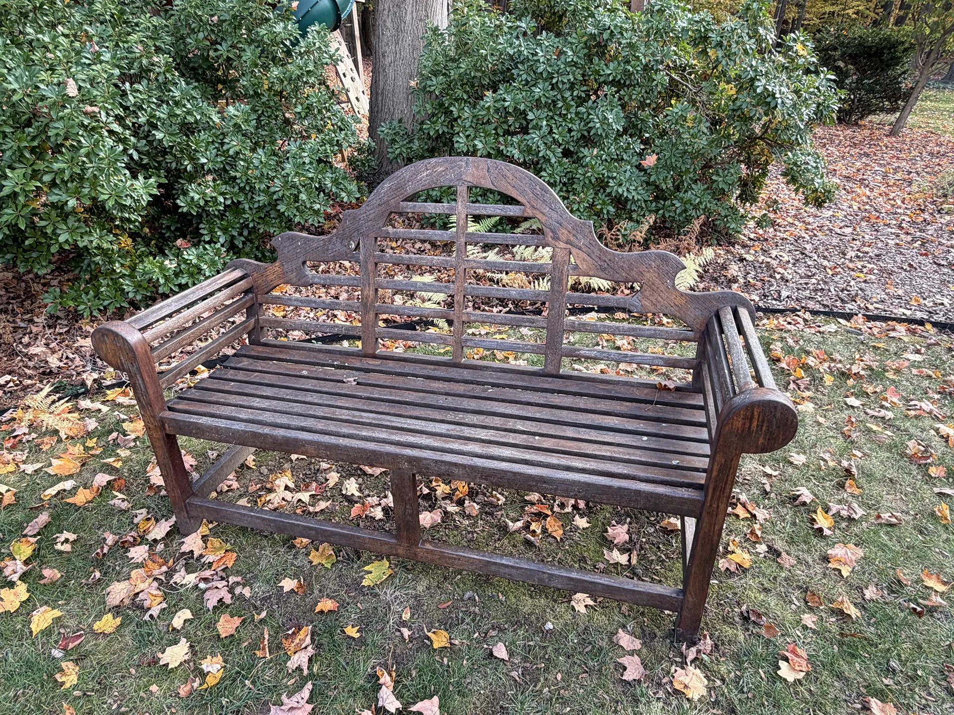 Wooden garden bench with decorative backrest surrounded by greenery.