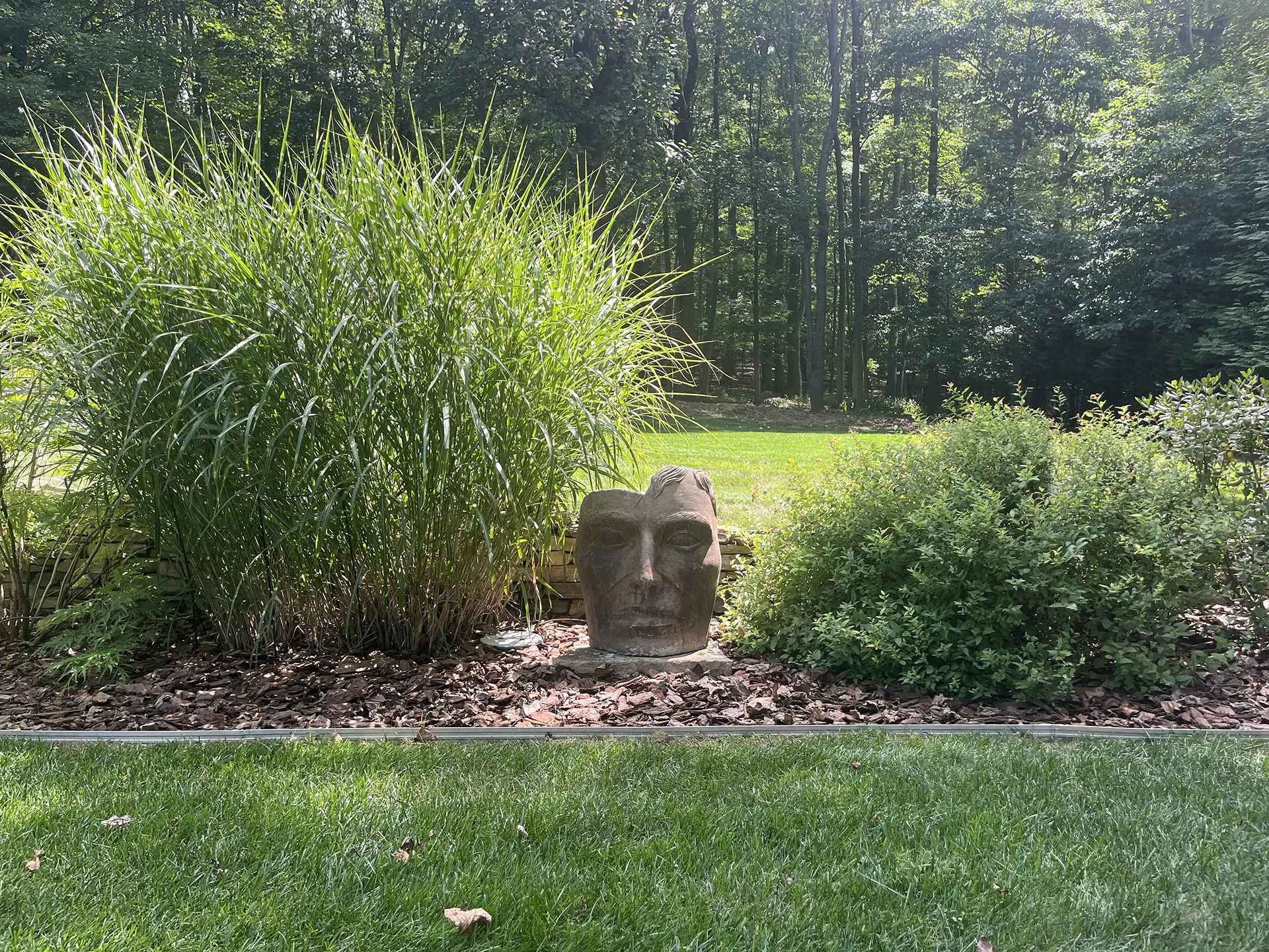 A stone face sculpture in a garden surrounded by greenery.