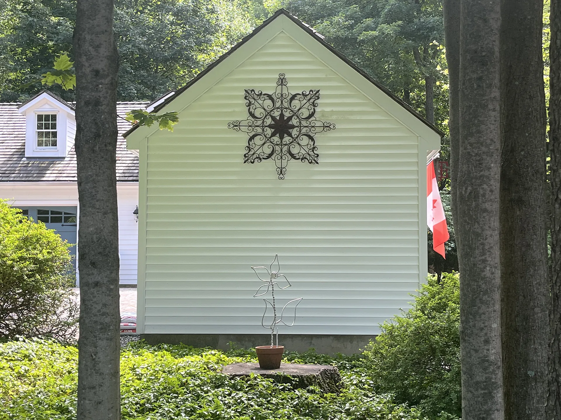 White house side with a decorative metal wall art and a potted plant.
