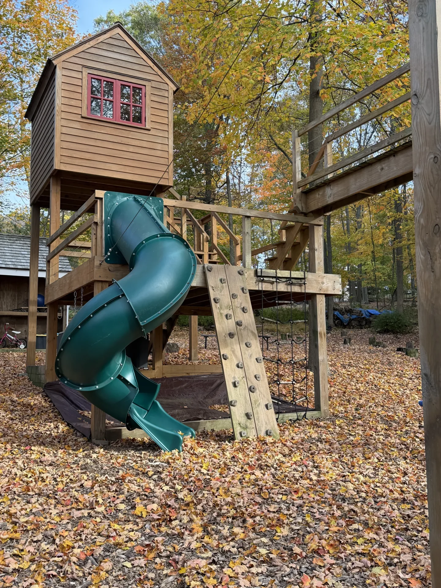 A wooden playground with a green spiral slide in a forested area.