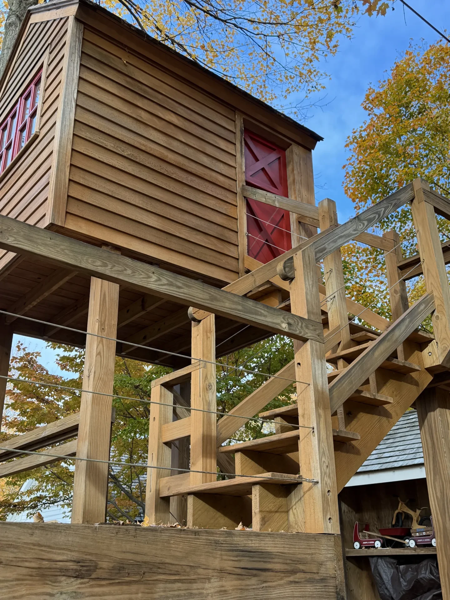 Wooden treehouse elevated with stairs and railing among autumn trees.