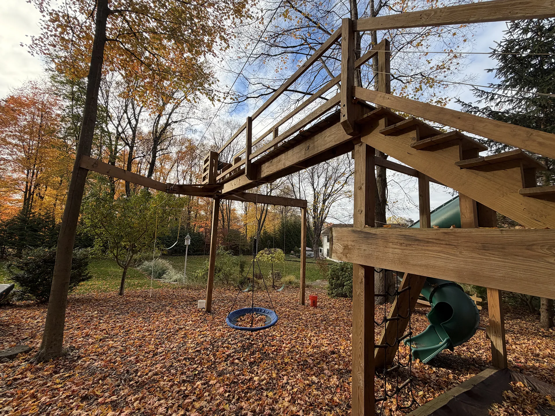 A wooden playground structure with a tire swing in an autumn yard.