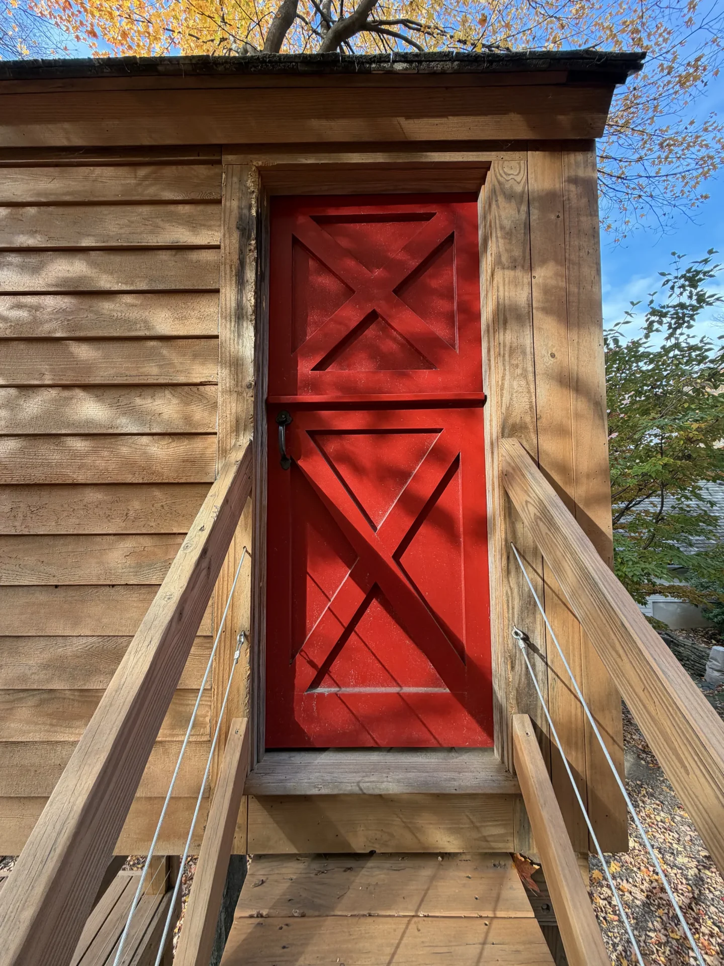 Red wooden door on a rustic building with wooden stairs.
