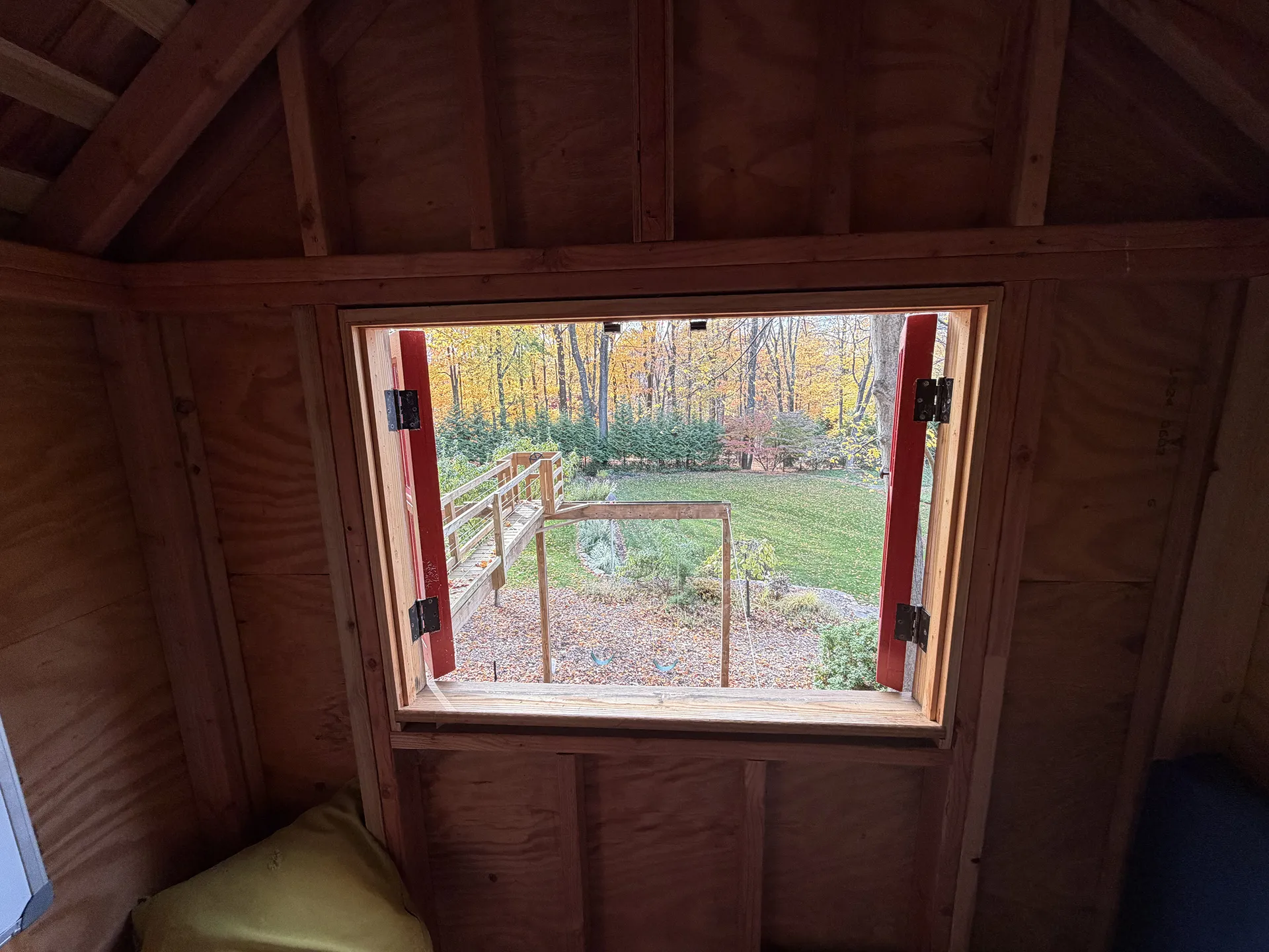 View from a wooden cabin window overlooking a garden with trees.