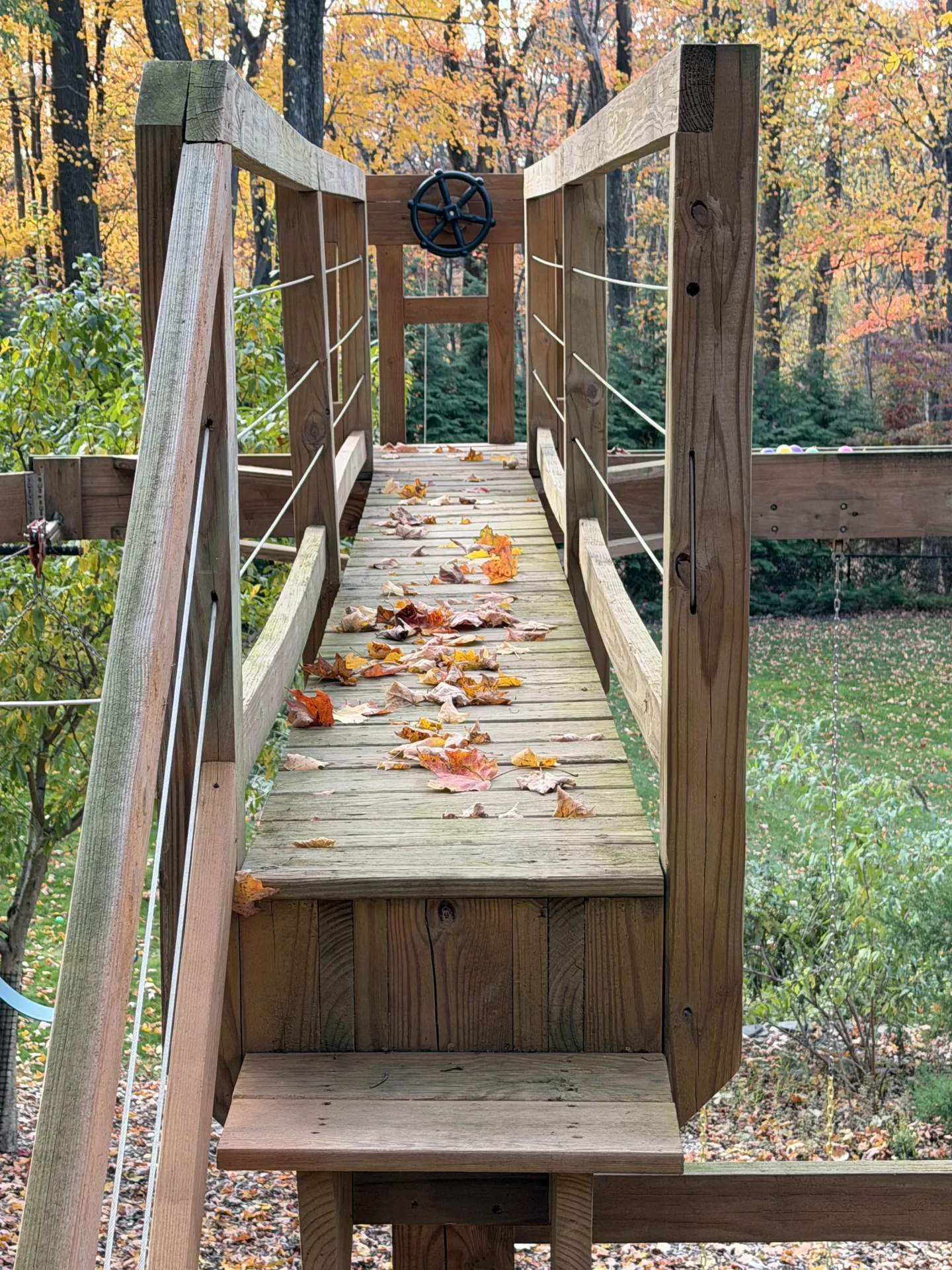 Wooden footbridge with autumn leaves scattered on it during fall.