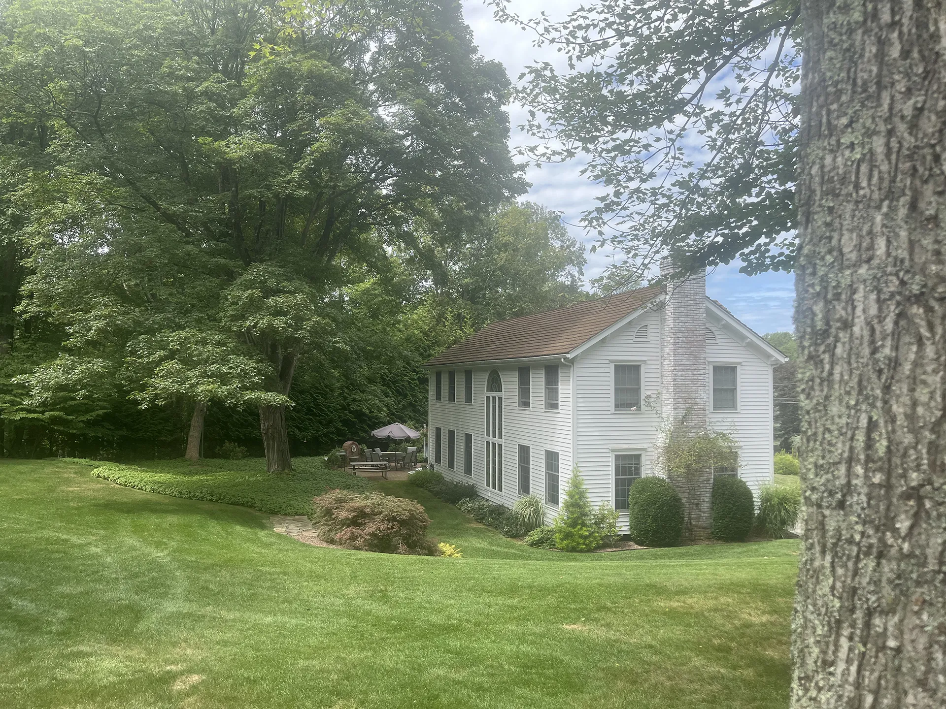 A quaint white two-story house surrounded by lush green trees and grass.