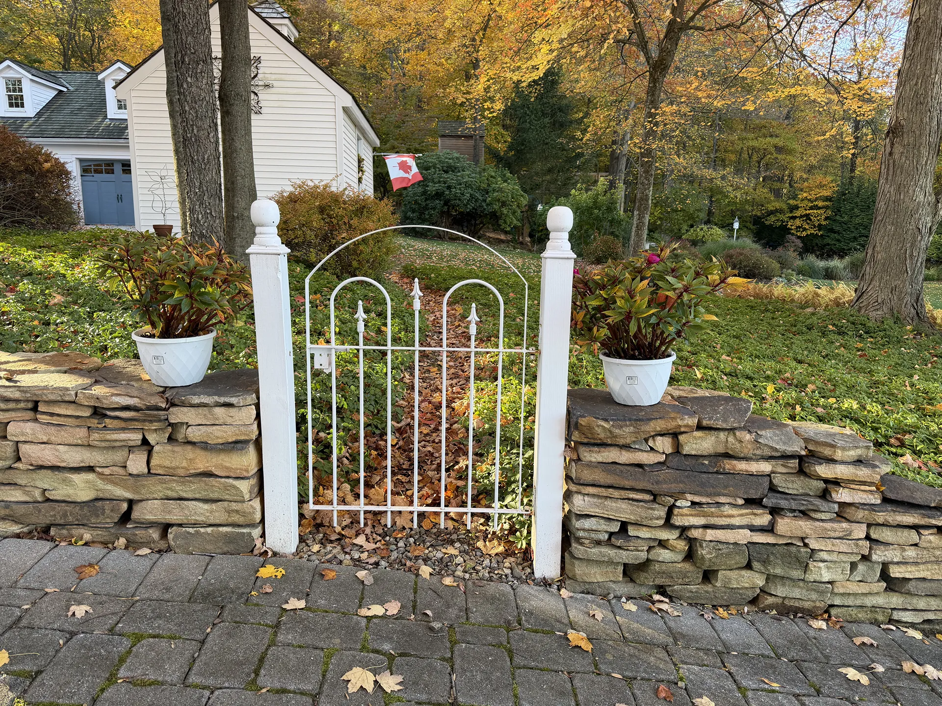 White garden gate in front of a stone wall with potted plants.