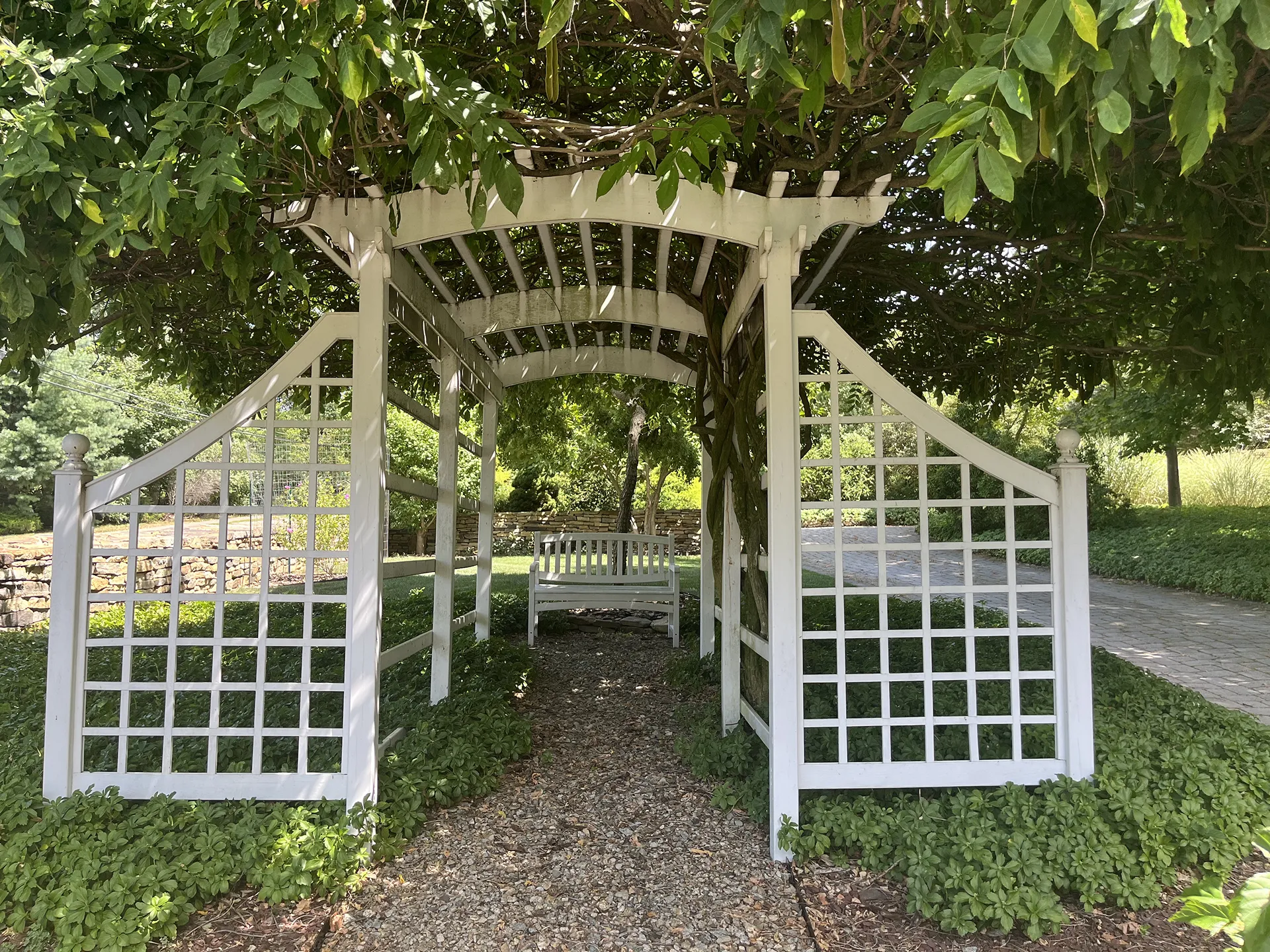 White wooden garden arbor with lattice panels and a gravel path.