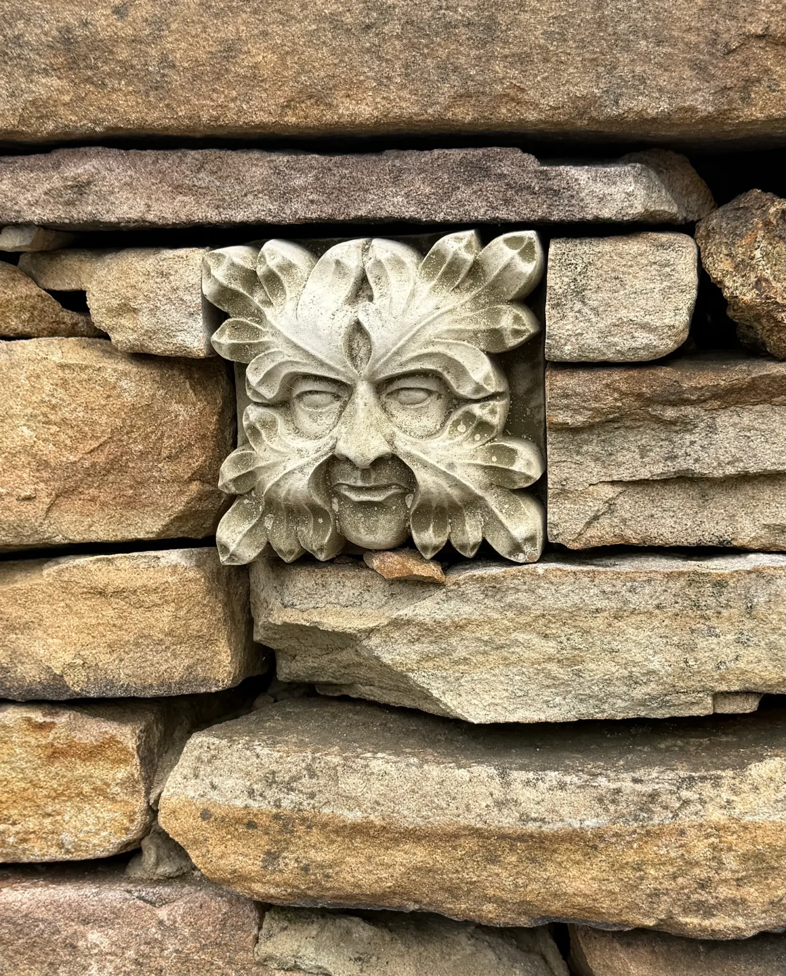Stone wall with a carved Green Man face embedded.