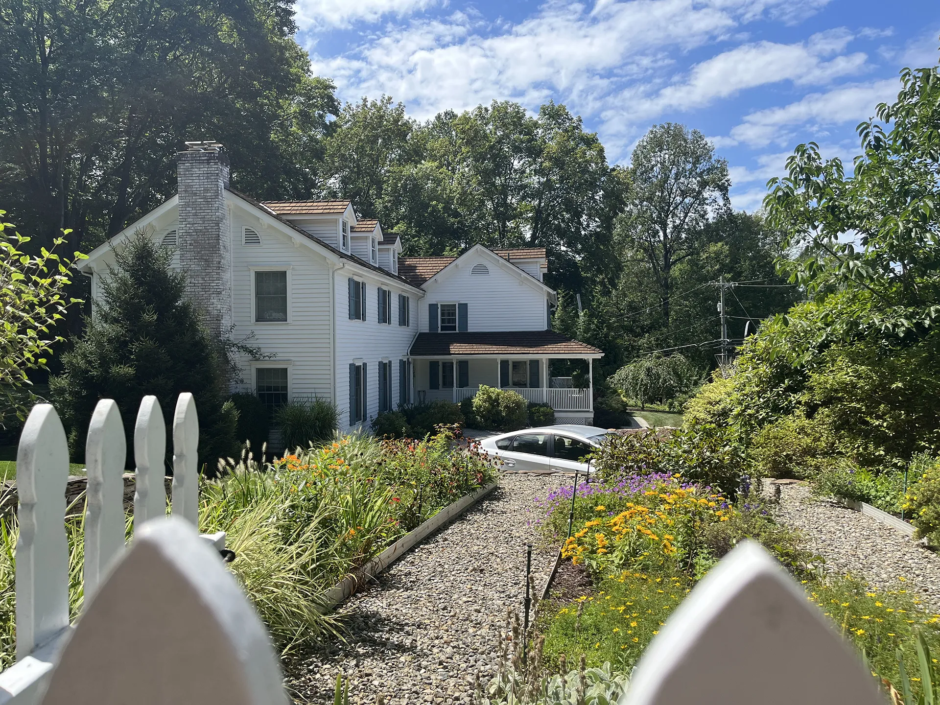 A charming white house surrounded by lush greenery and flowers under a blue sky.