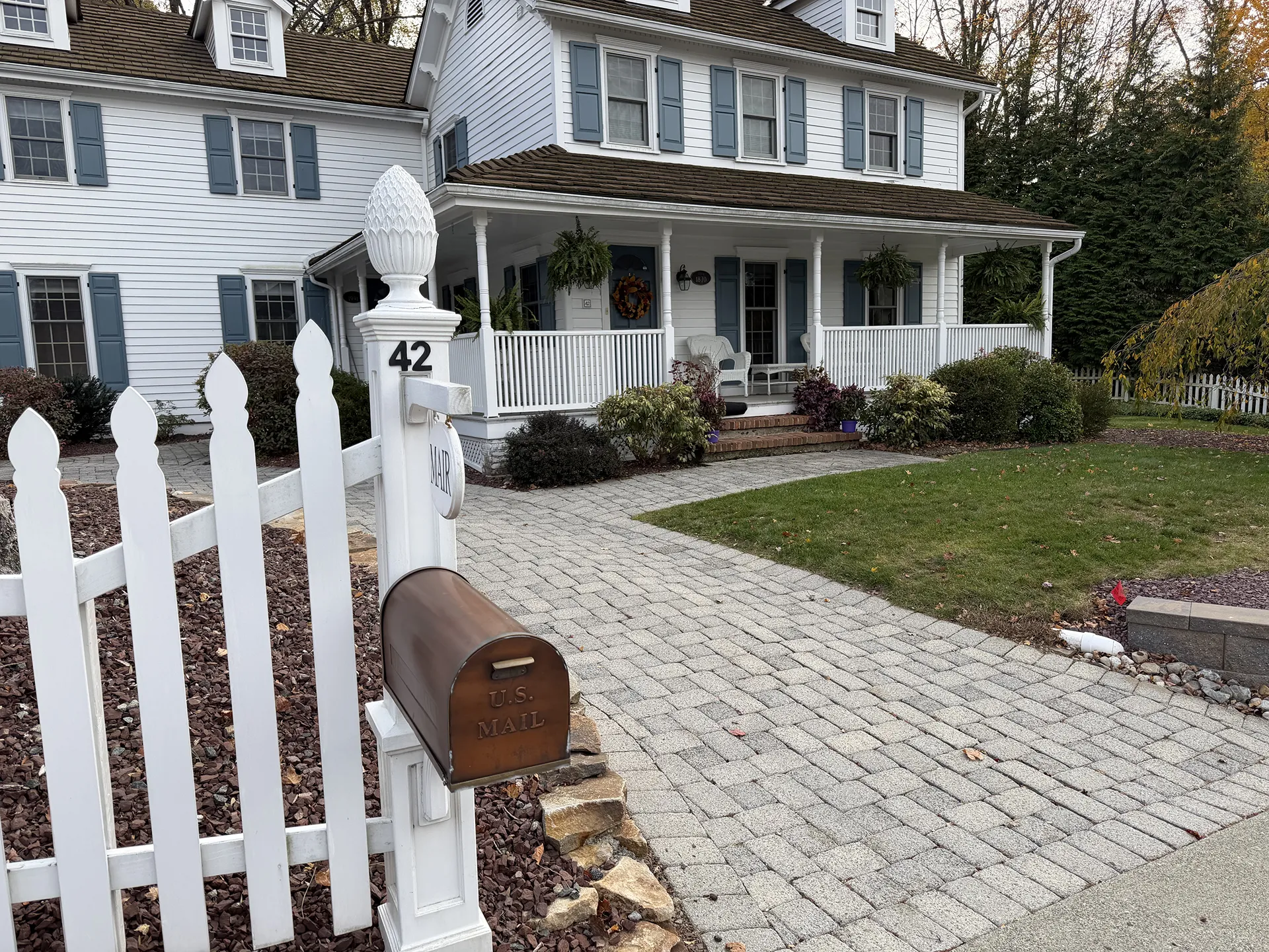 White mailbox and house with number 42 on a post by a white picket fence.