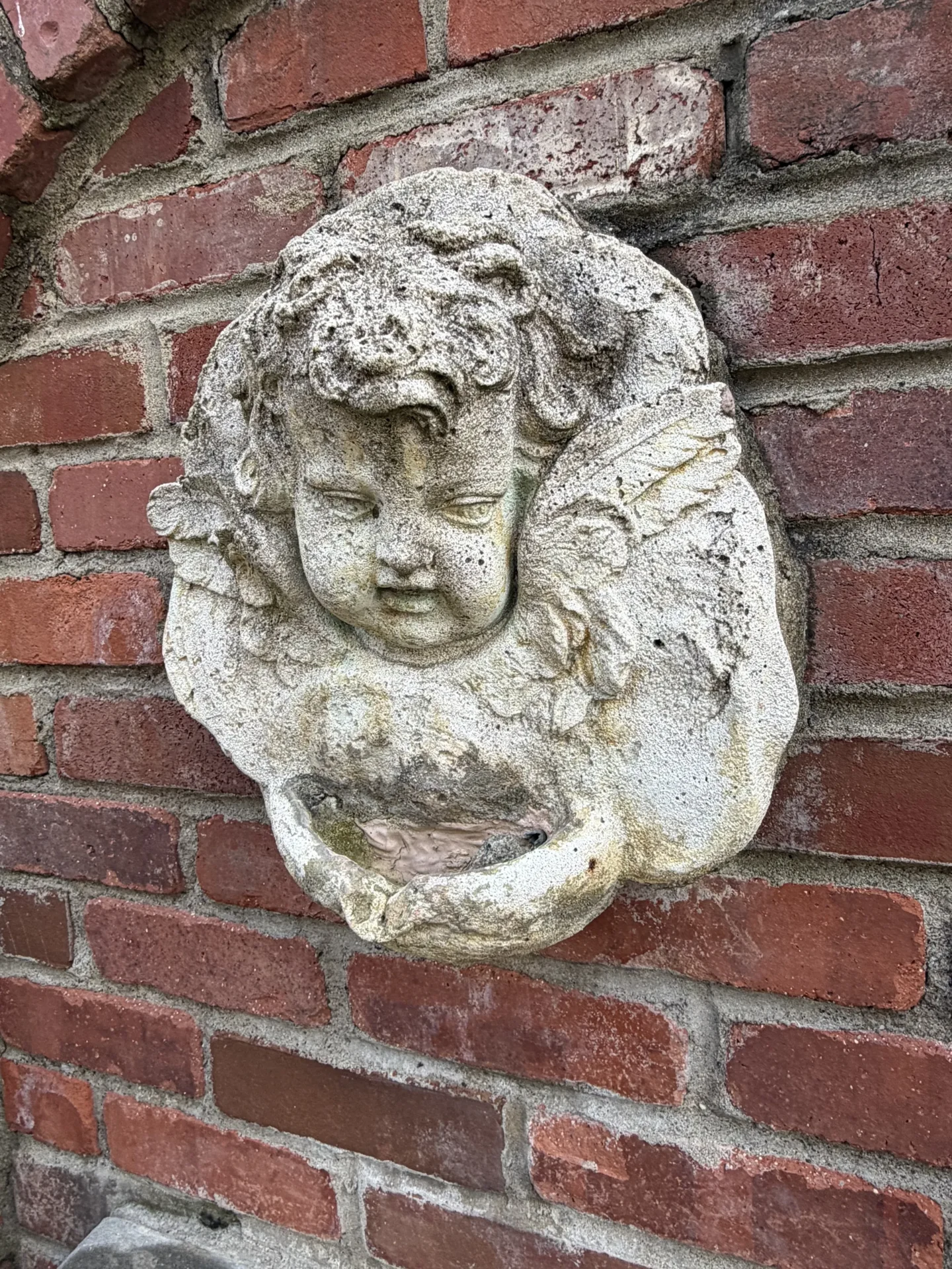 Stone cherub sculpture mounted on a red brick wall.