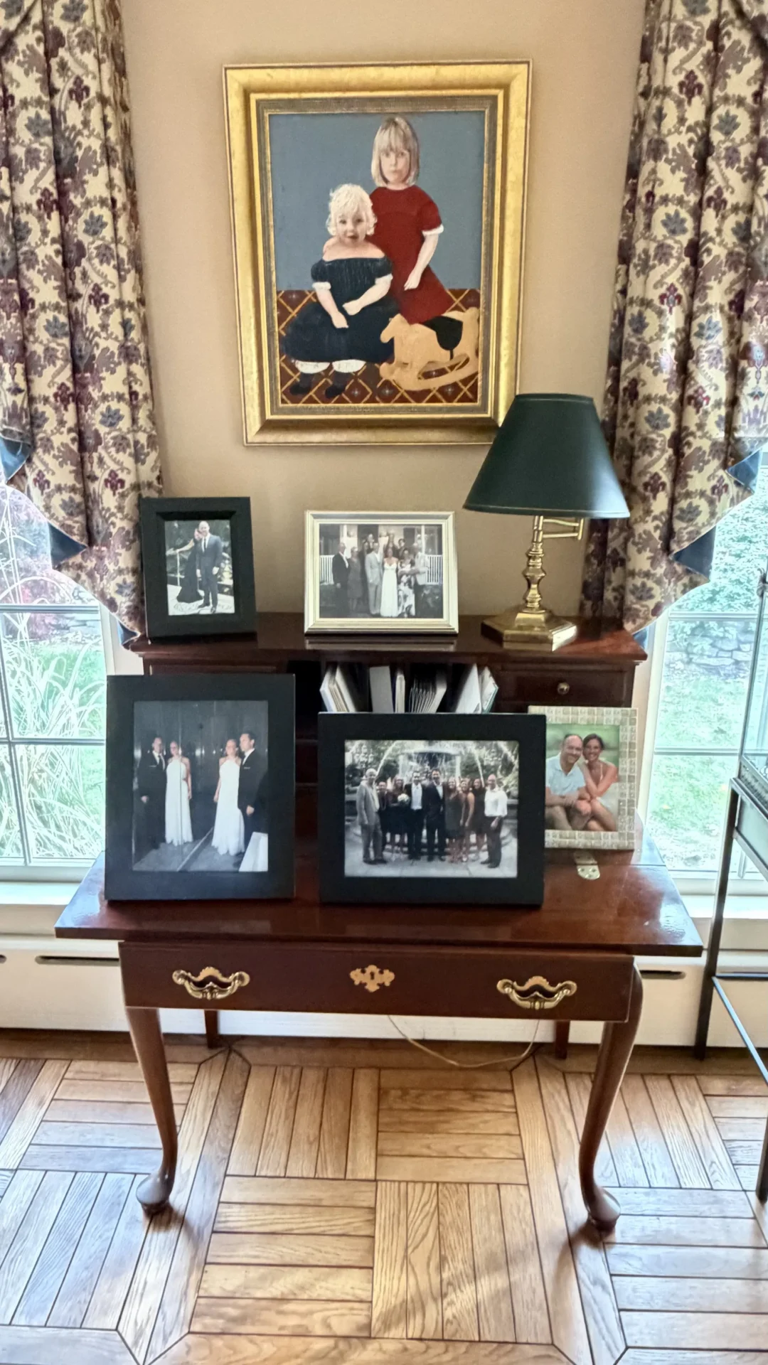 A wooden table with framed black-and-white photos and a lamp near a window.