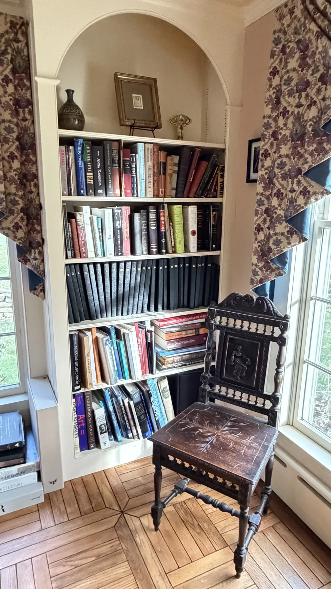 A bookshelf filled with books and records next to a wooden chair.