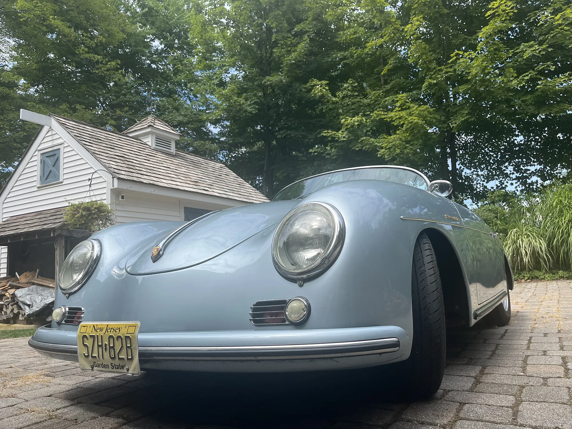 A classic silver Porsche 356 parked on a driveway.