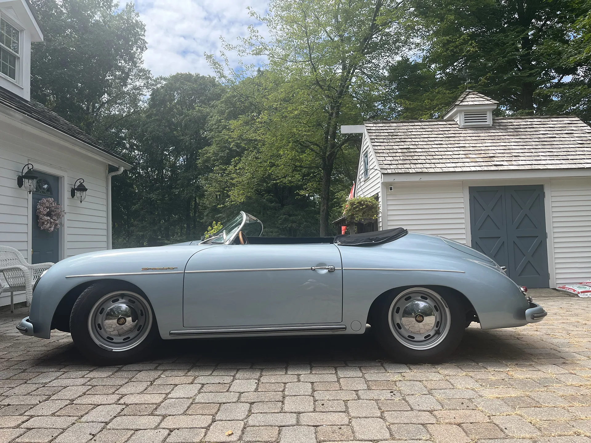 Classic silver convertible car parked on a stone driveway beside garages.