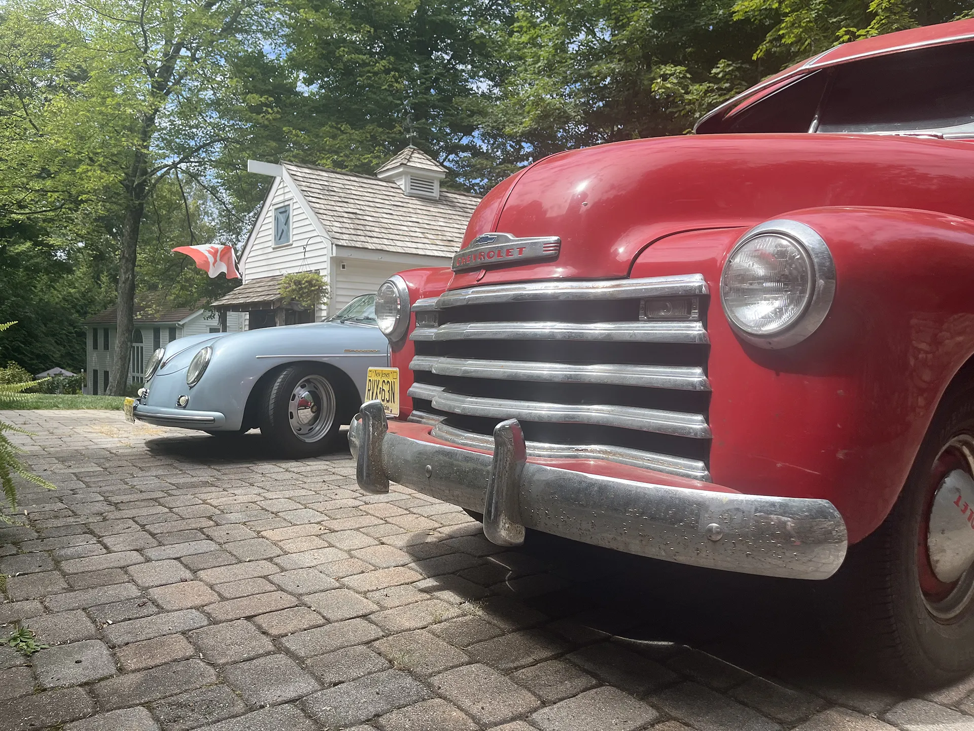 Two vintage cars parked on a cobblestone driveway surrounded by greenery.