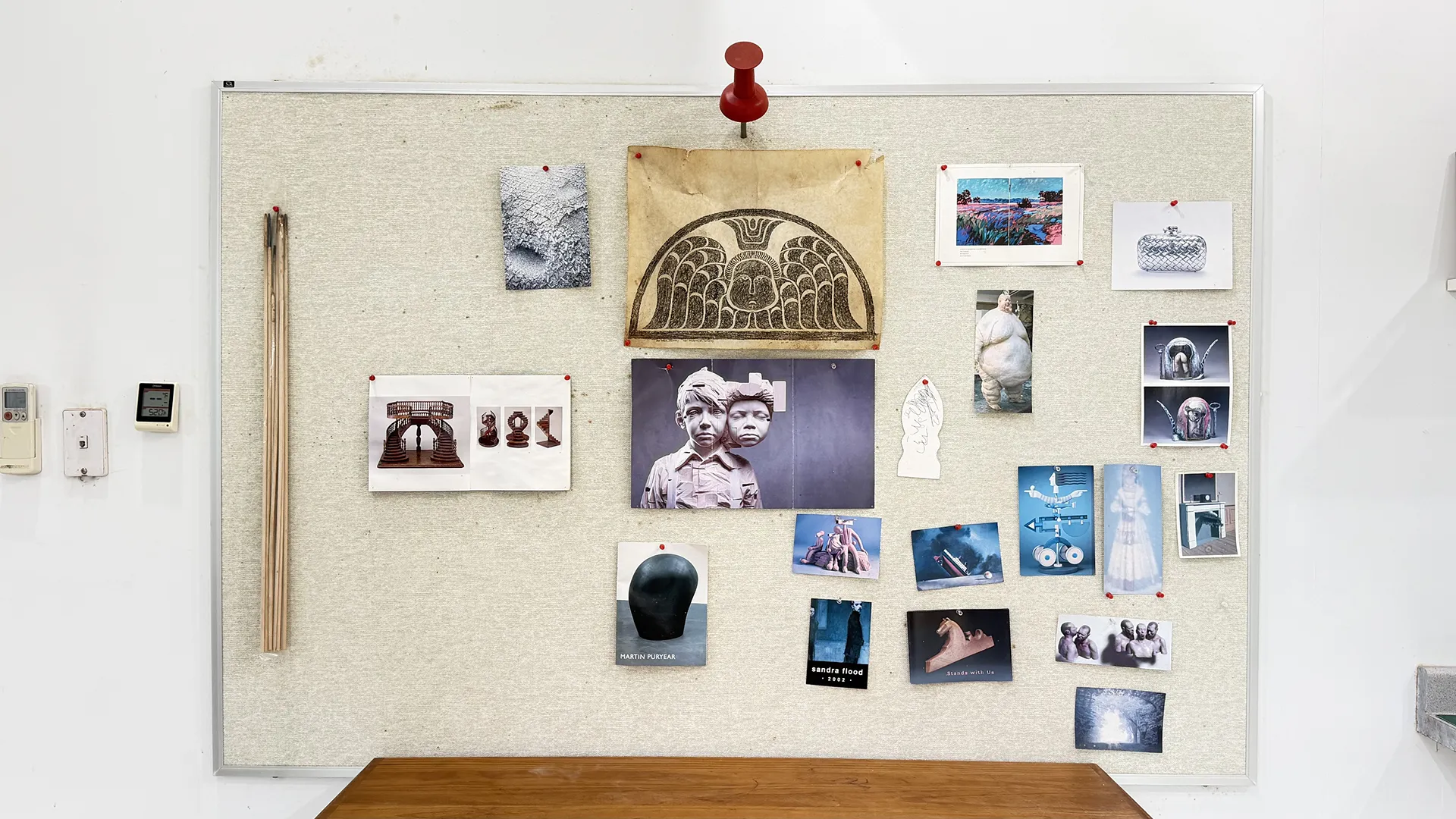 A bulletin board filled with various photos and postcards pinned above a wooden desk.