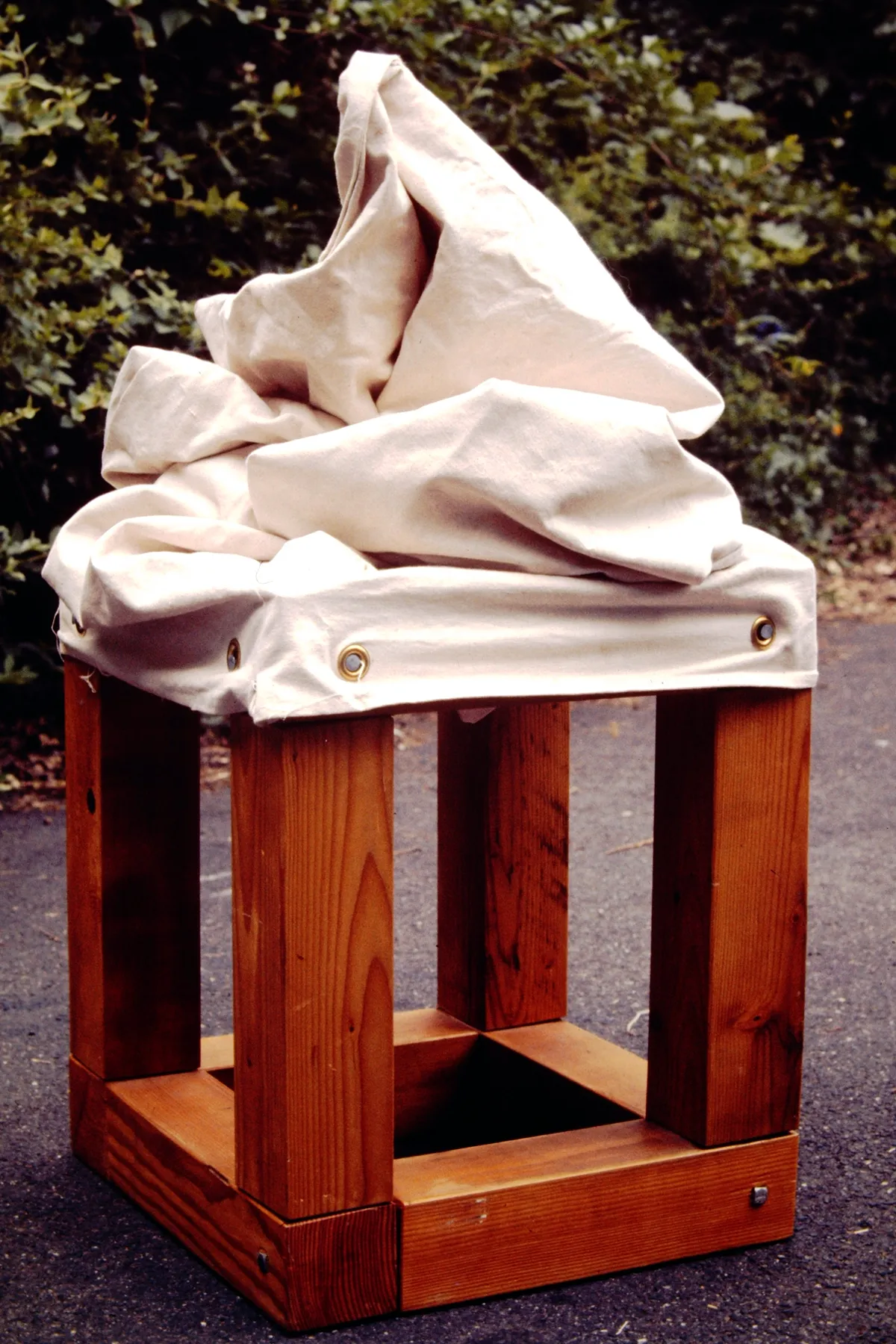 A wooden stool with a white, abstract fabric sculpture on top.