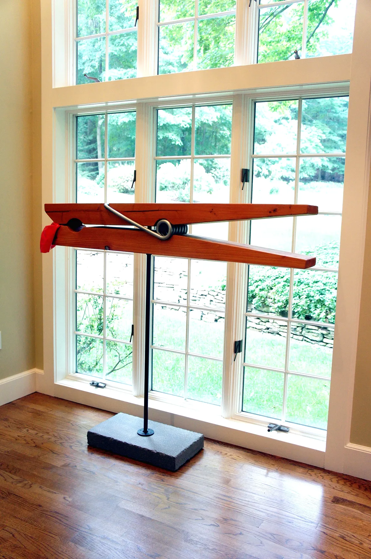 Large wooden clothespin sculpture on a stand in front of a window.
