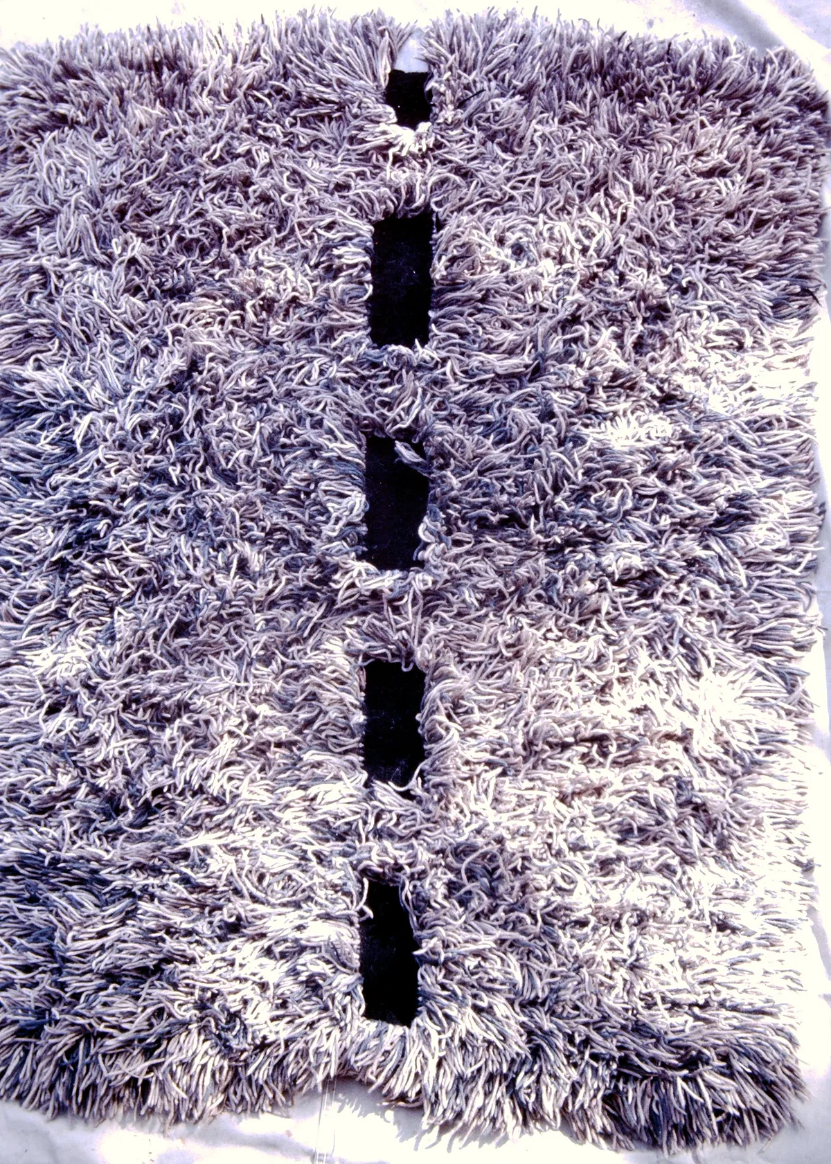 Close-up of a textured gray carpet with a row of black rectangular holes.