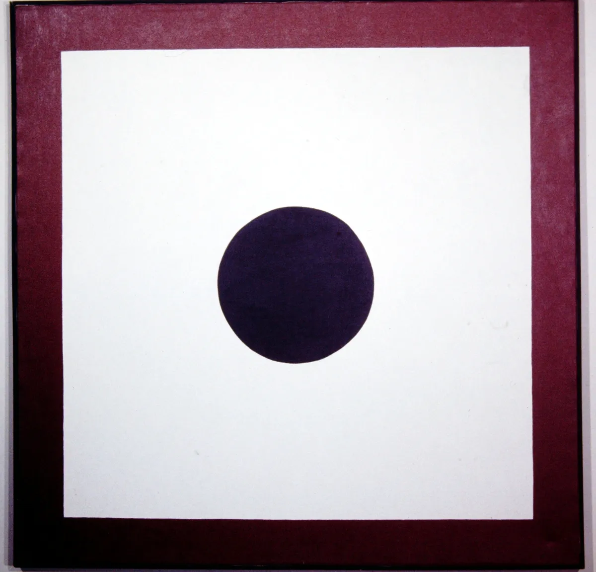 A black circle centered on a white square with a brown frame.