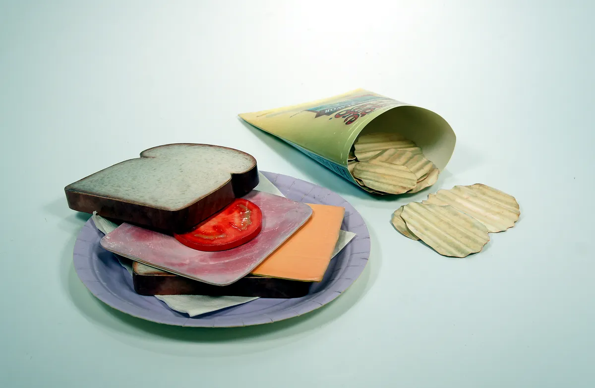 An open sandwich with layers of bread, cheese, tomato, and lettuce beside a bag of potato chips.