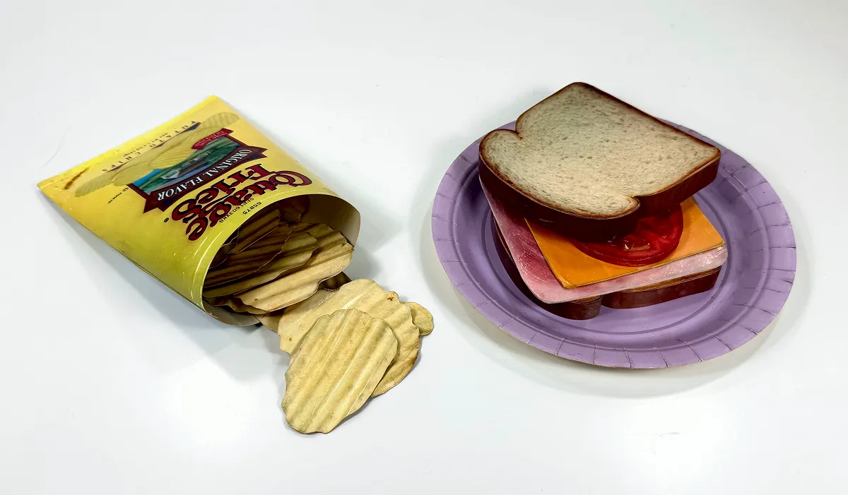 A sandwich with cheese and deli meat beside a fish-shaped cracker container.