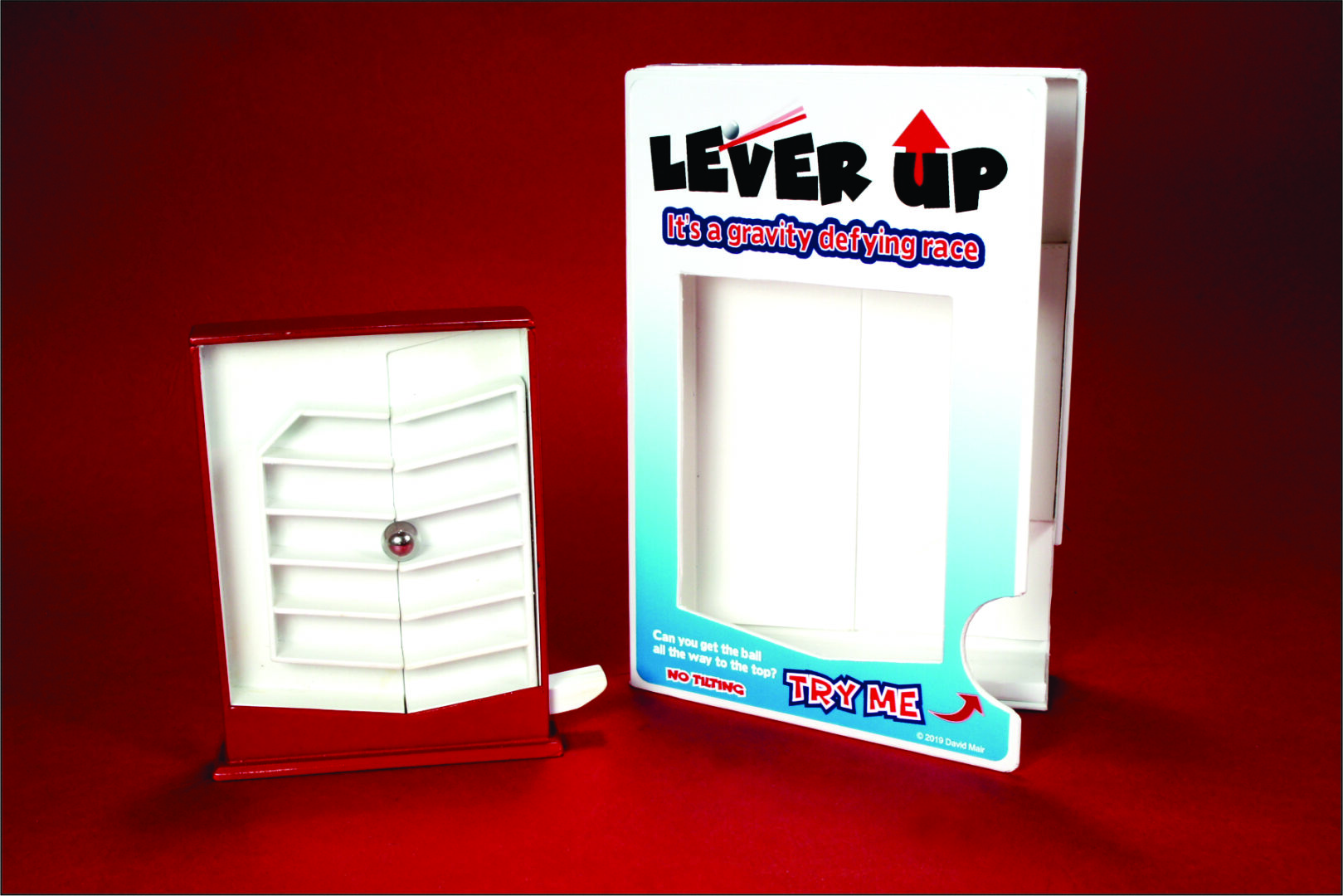 A white plastic lever-up device next to its colorful packaging box.